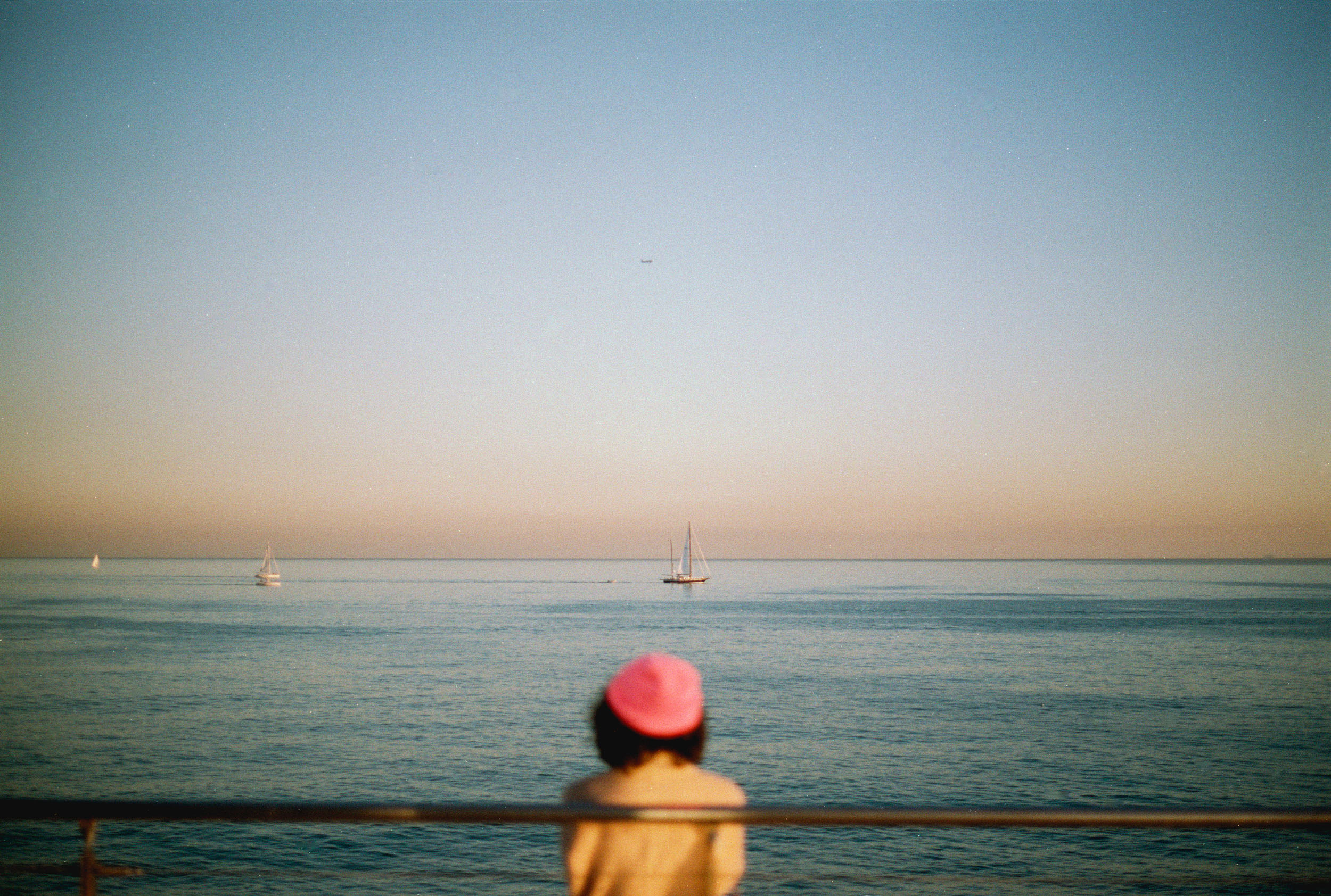 Seascape at sunset with a person in the foreground wearing a pink bucket hat