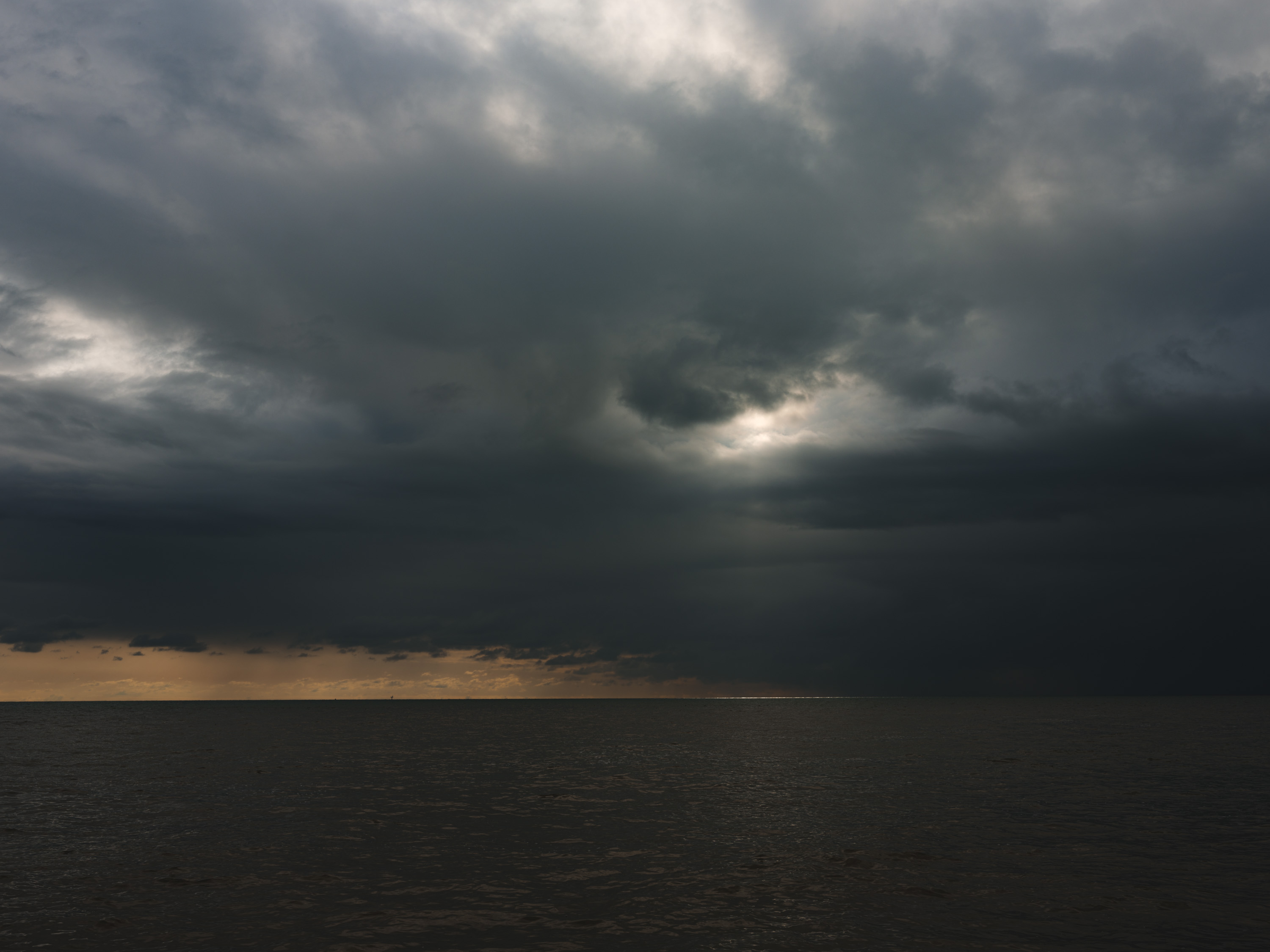 Moody seascape with small light shining through the clouds. Shot with Fuji GFX100.
