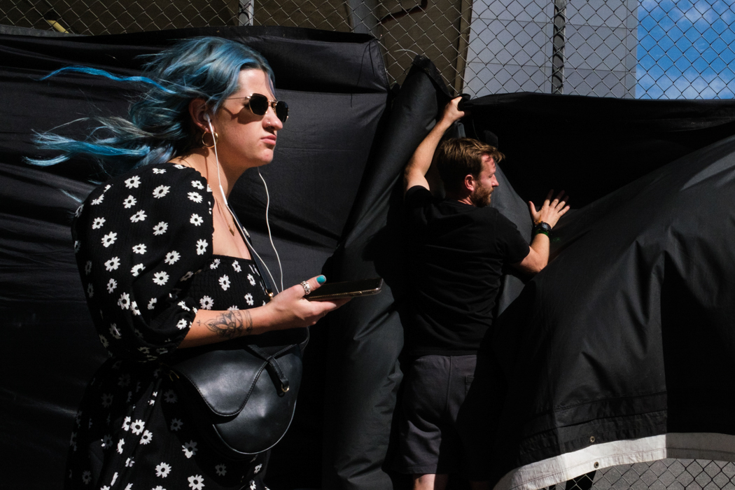 Person mit blauen Haaren und Sonnenbrille unterwegs mit Kopfhörern 