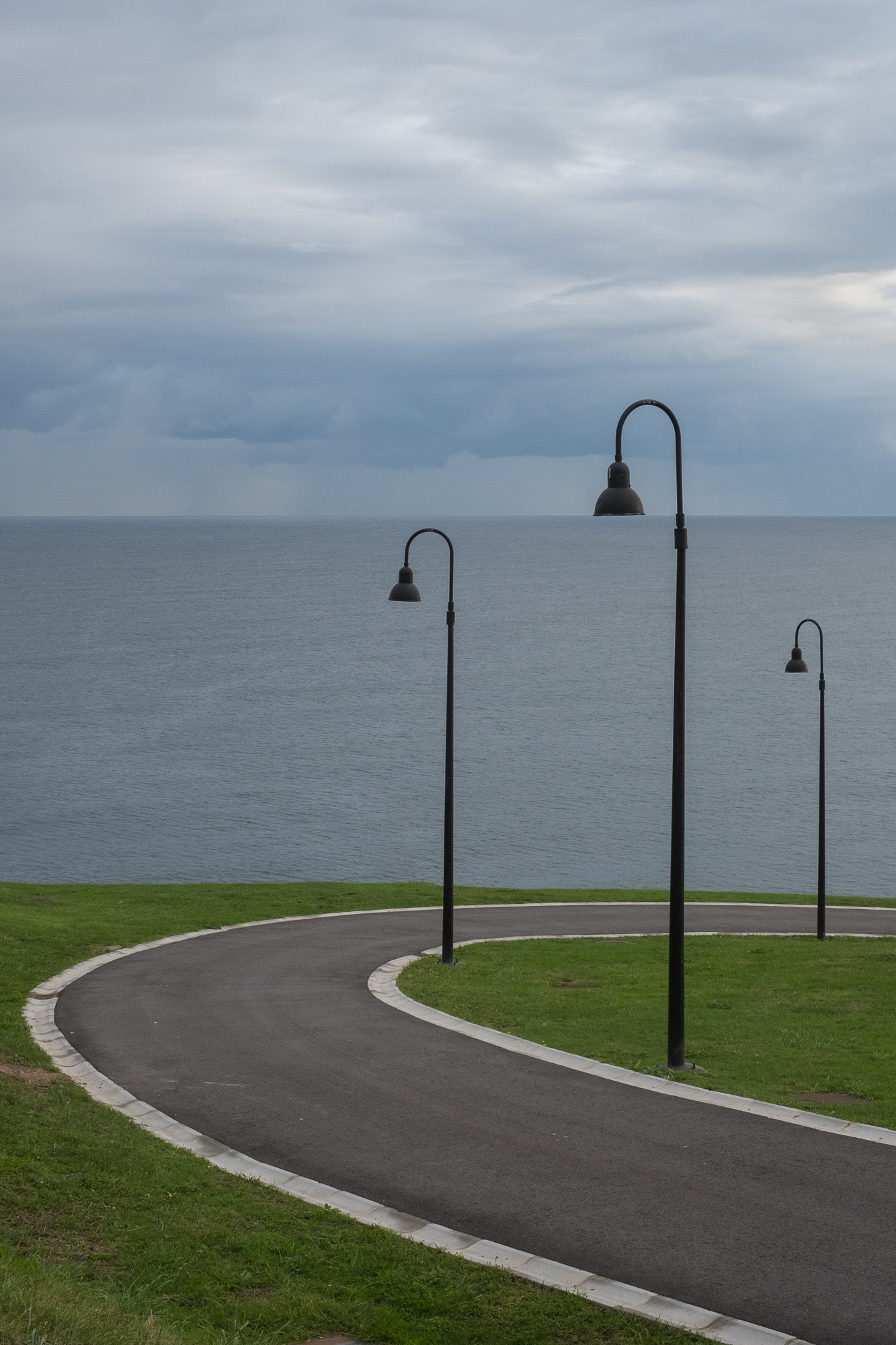Streetlights on a curving road line up perfectly with the distant horizon line of the sea