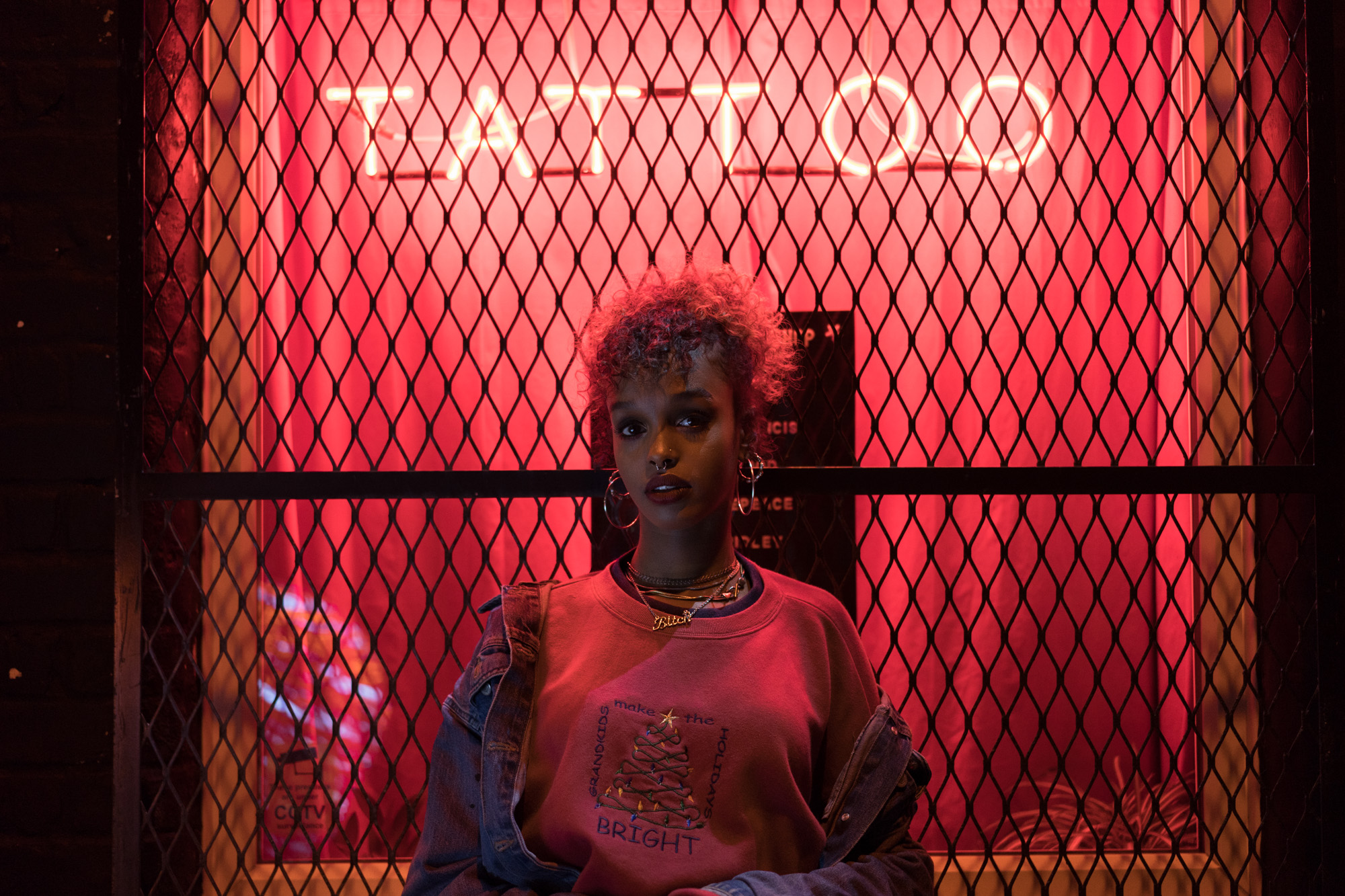 Low-light portrait photo of a model, with illuminated red tattoo sign in background, shot with Sony A9