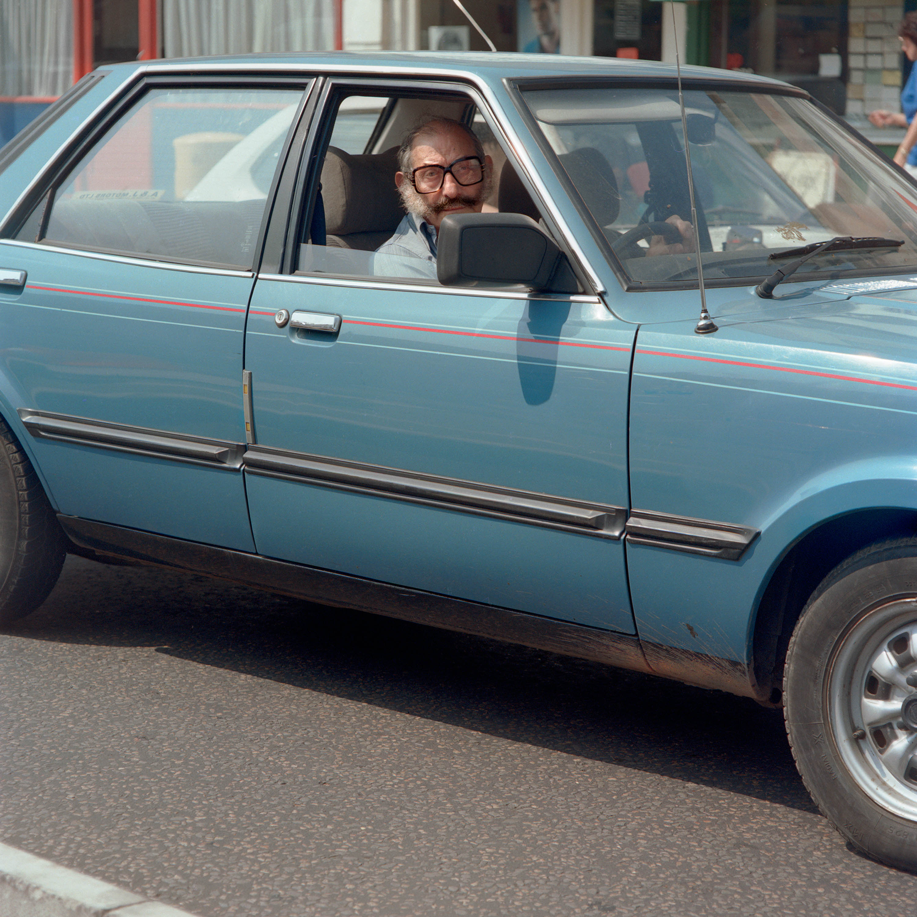 Man with interesting facial hair in a vintage blue car in East London 