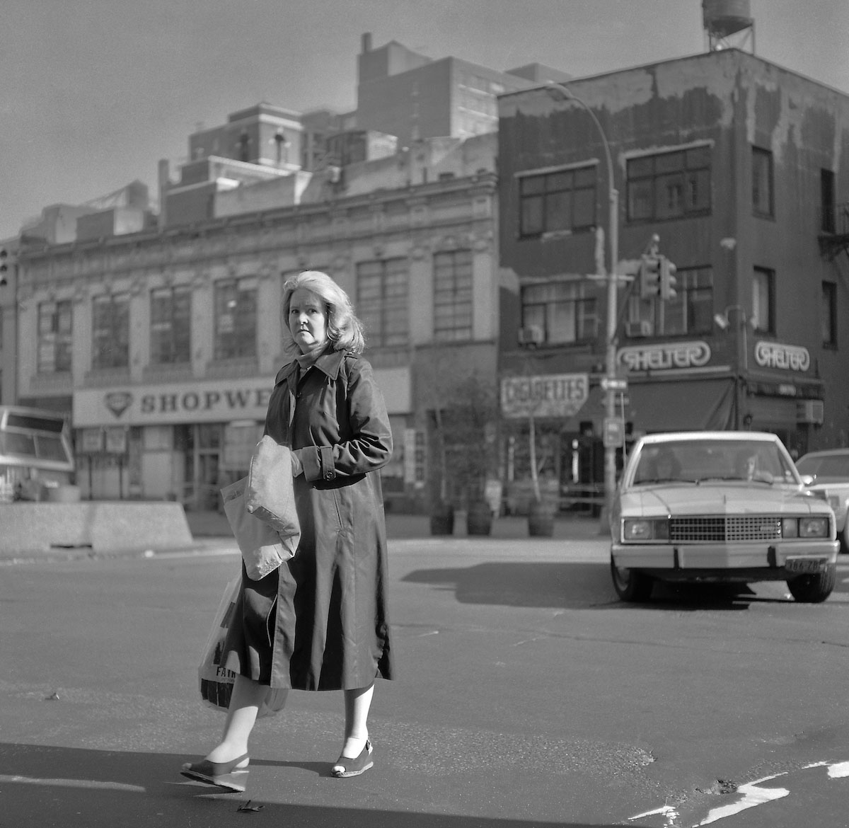 lady crossing road 70's B&W - moving car in the background in the USA.