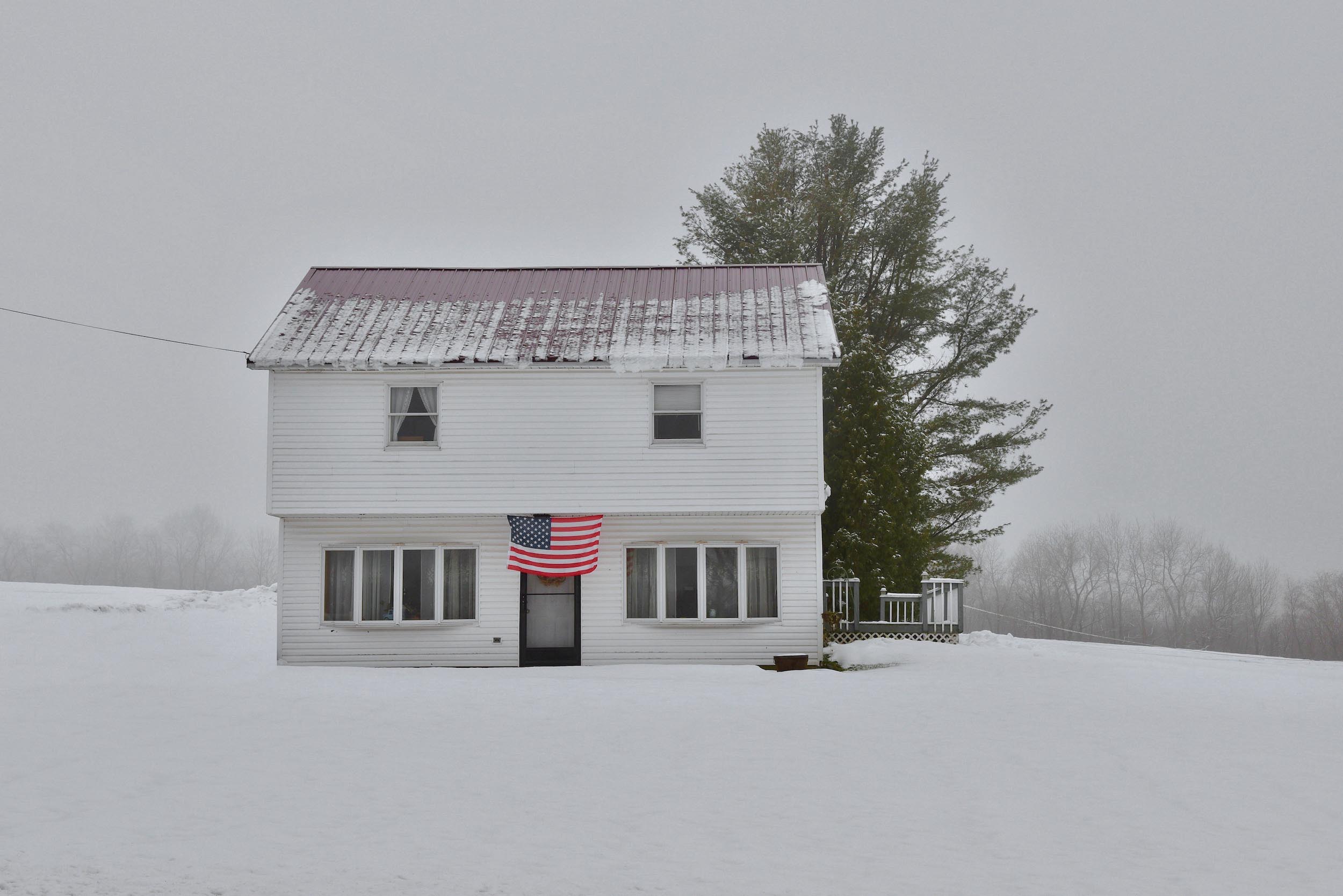 A white house in the snow with a USA flag hung over the doorway