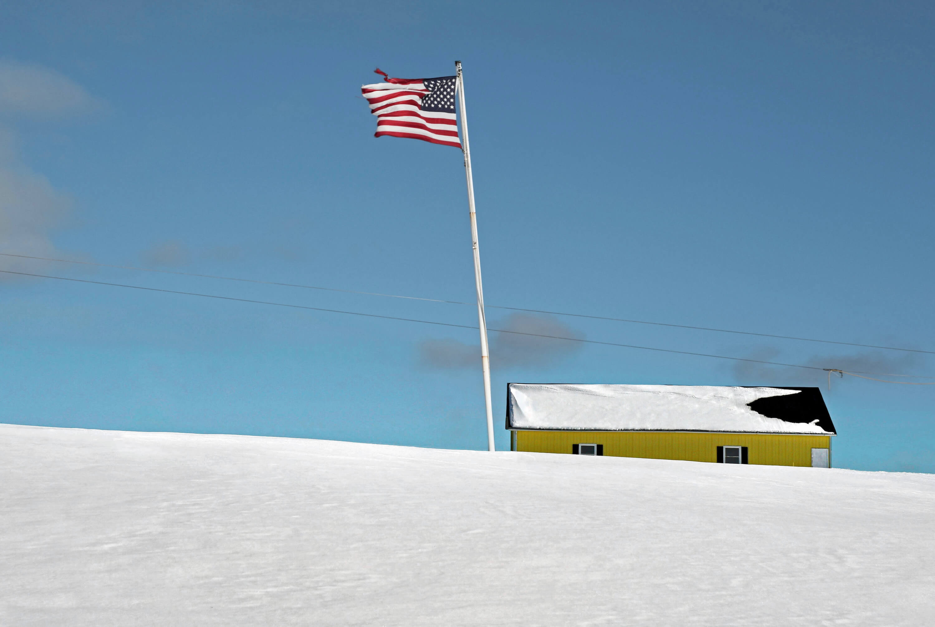 House on a hill in the snow with a USA flag on a pole.