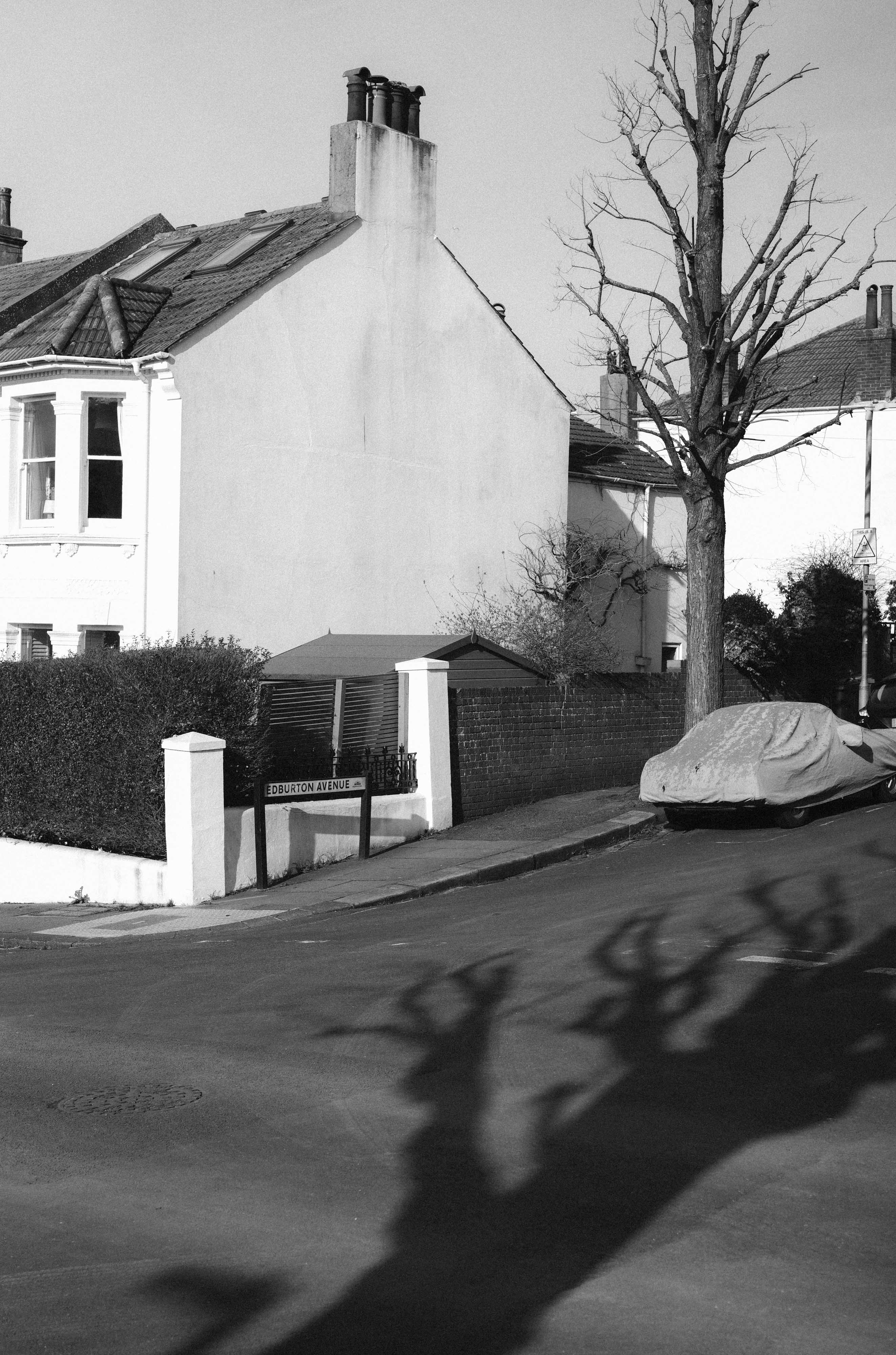 Une photo en noir et blanc d'une maison, d'une voiture et d'un arbre, prise à la lumière du jour avec un Leica M10 Monochrom et un ISO faible.