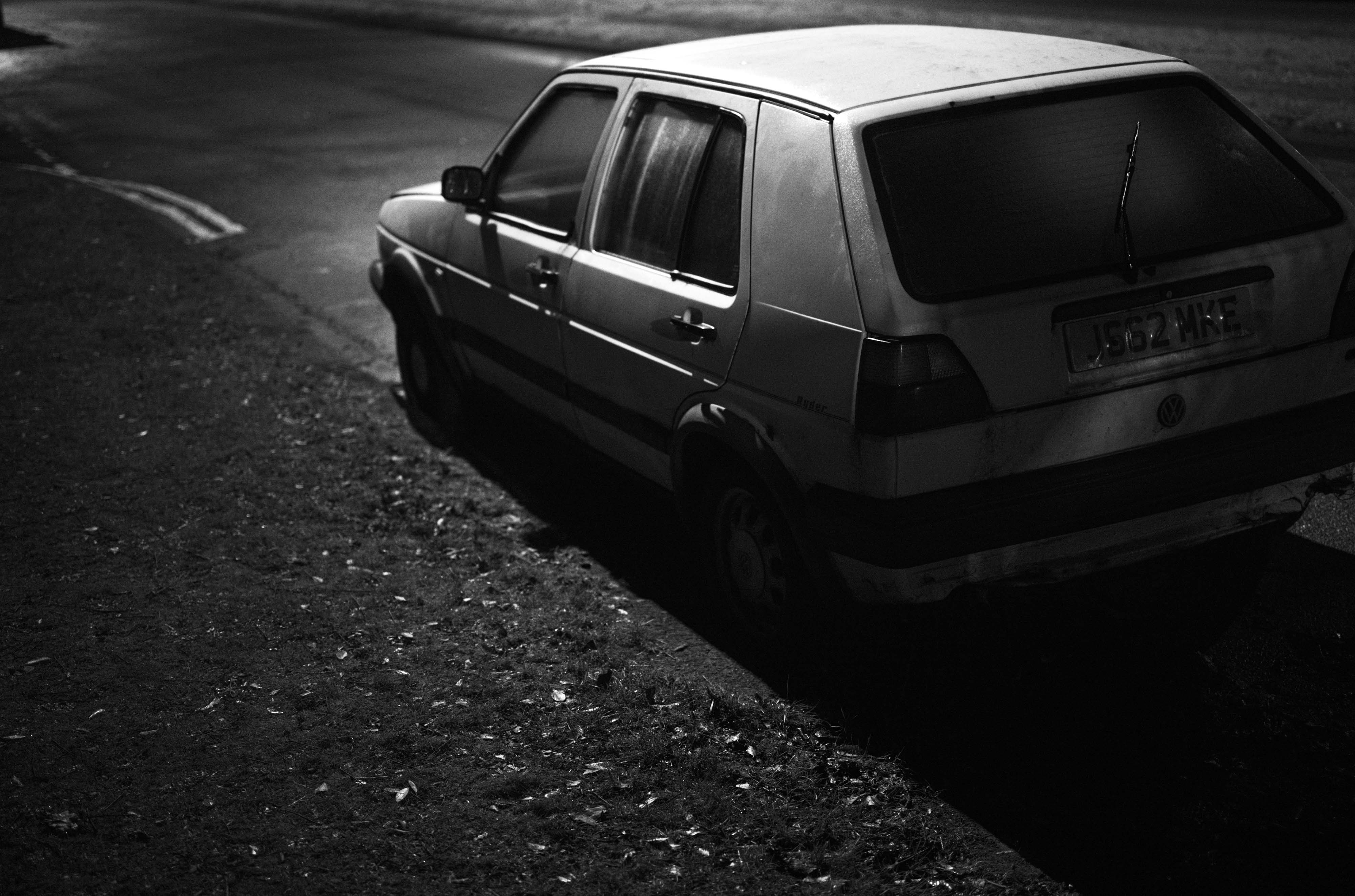 Ein Schwarz-Weiß-Foto von einem weißen Auto bei Nacht, das auf einer Straße geparkt ist, aufgenommen mit einer Leica M10 Monochrom