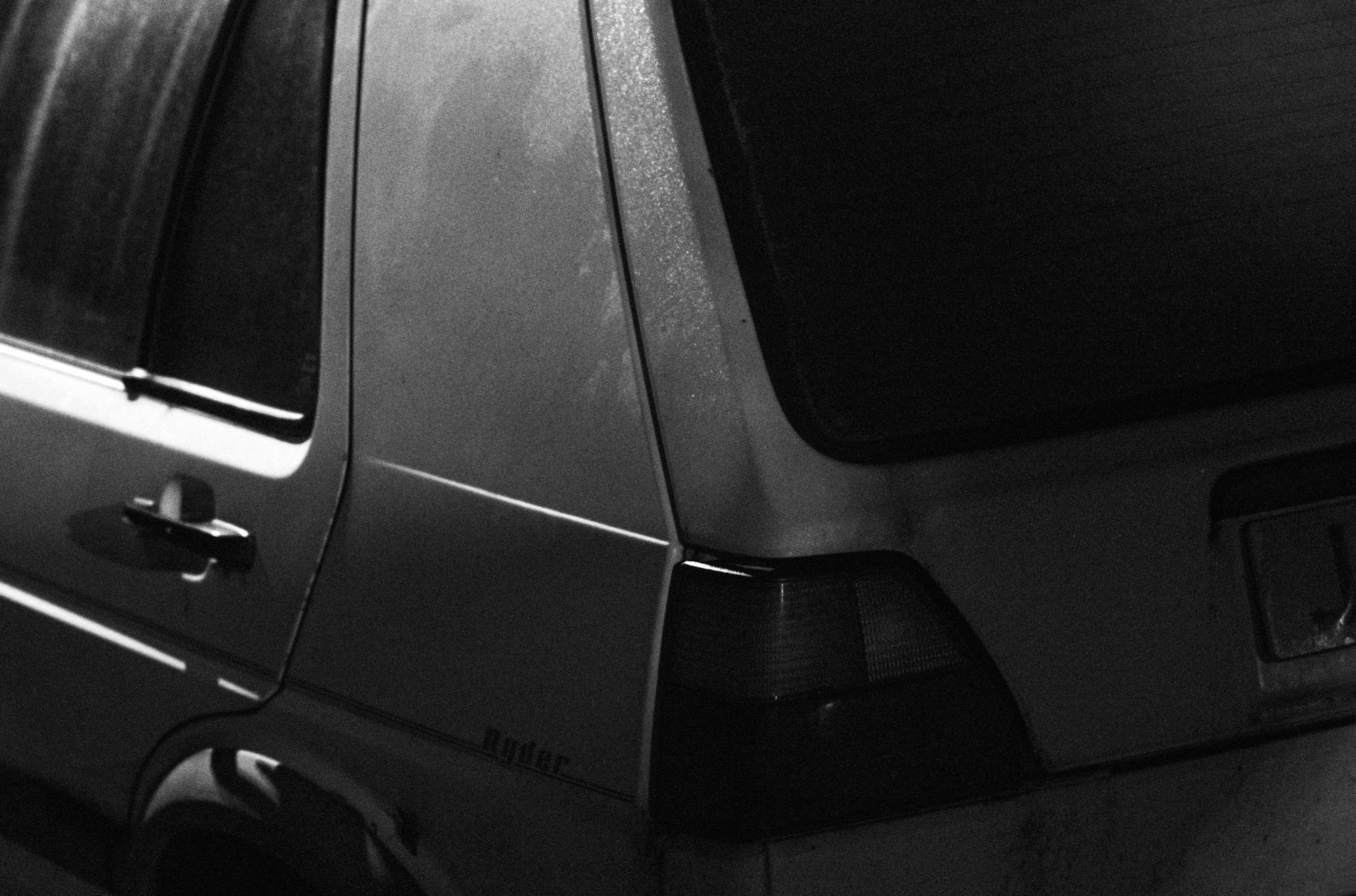 Photo recadrée en noir et blanc d'une voiture blanche garée de nuit sur une route derrière des lignes double-jaunes, prise avec un Leica M10 Monochrom.