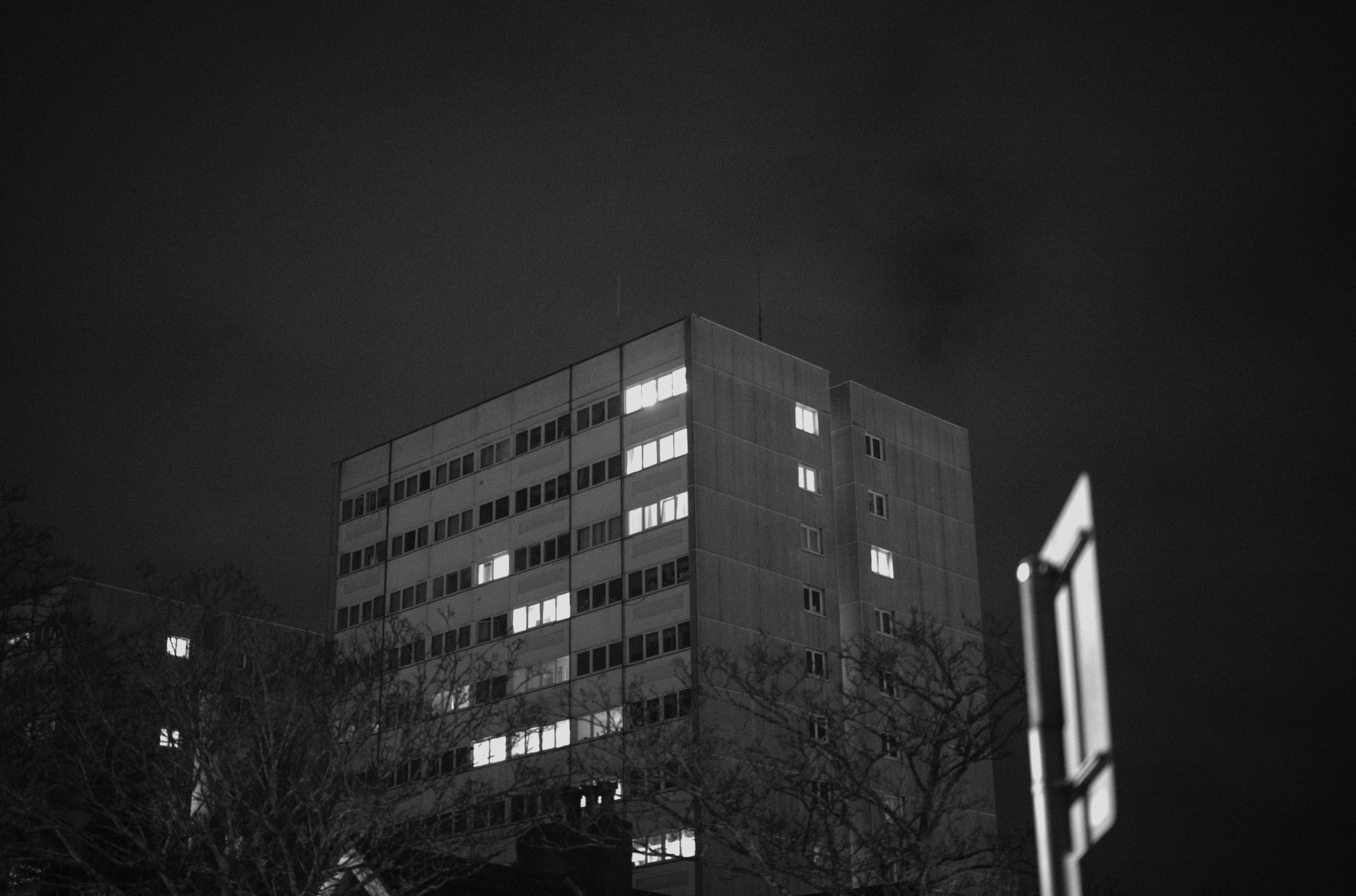 Une photo en noir et blanc d'une tour d'habitation la nuit, quelques fenêtres sont éclairées, prise avec un Leica M10 Monochrom à 64 000 ISO.