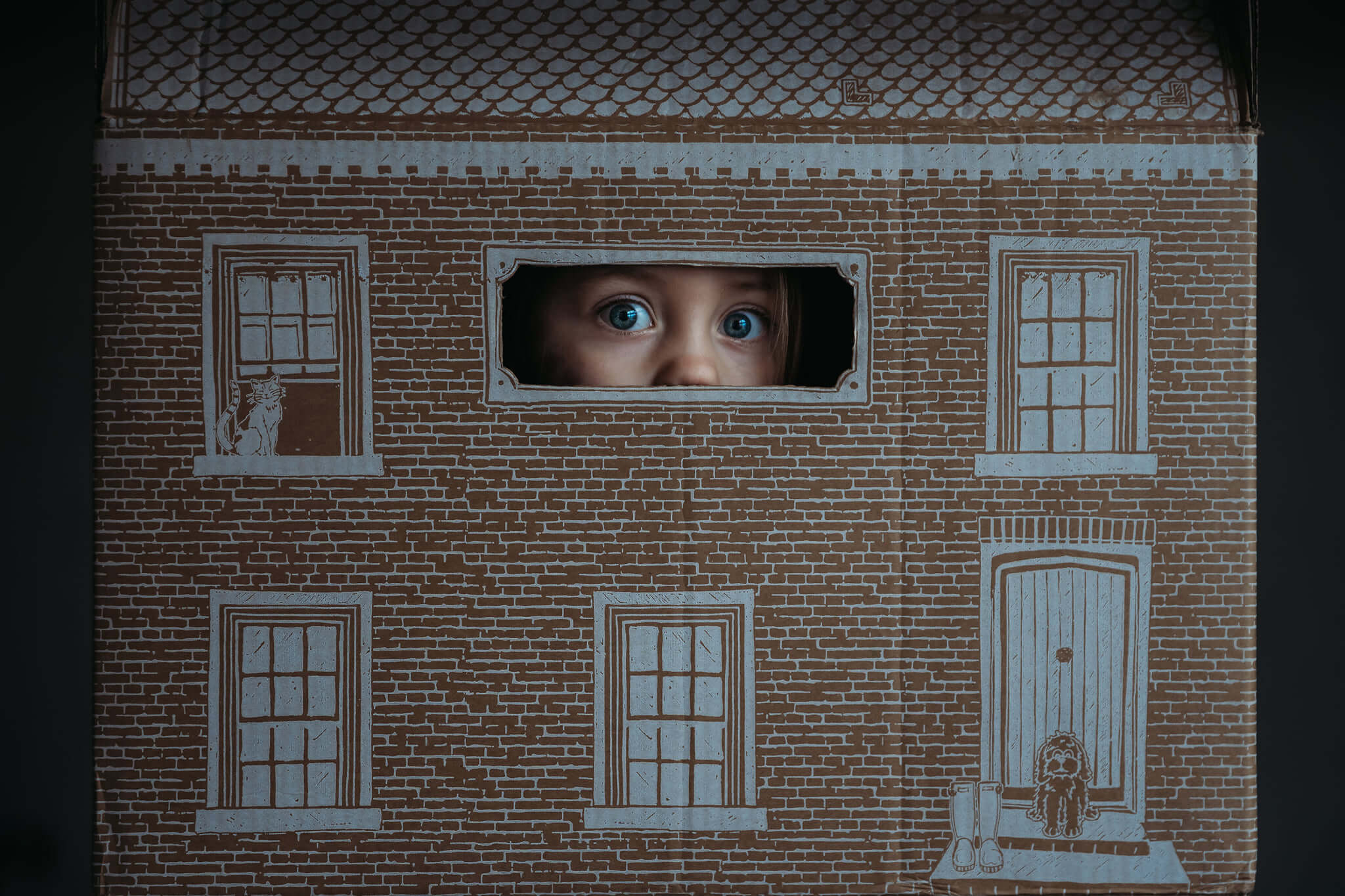 A kid looking through a cardboard house