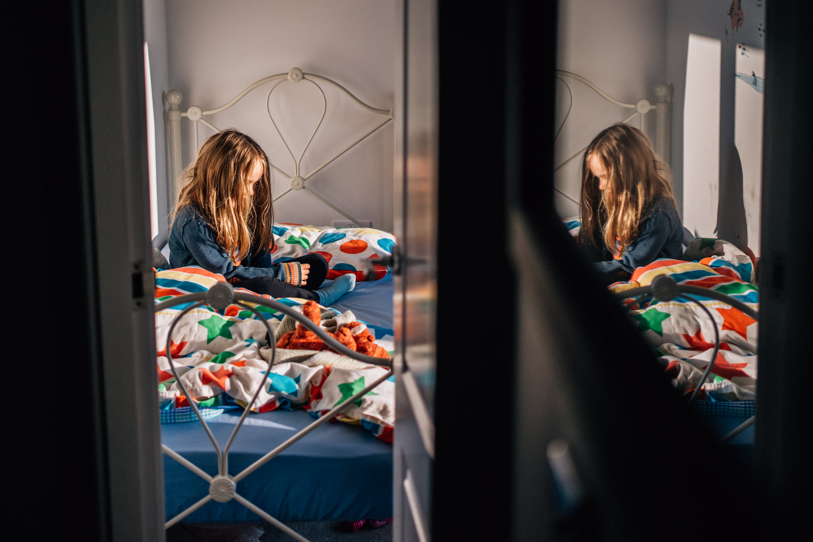 A child sitting in their bed, reflected by the glass pane of a door