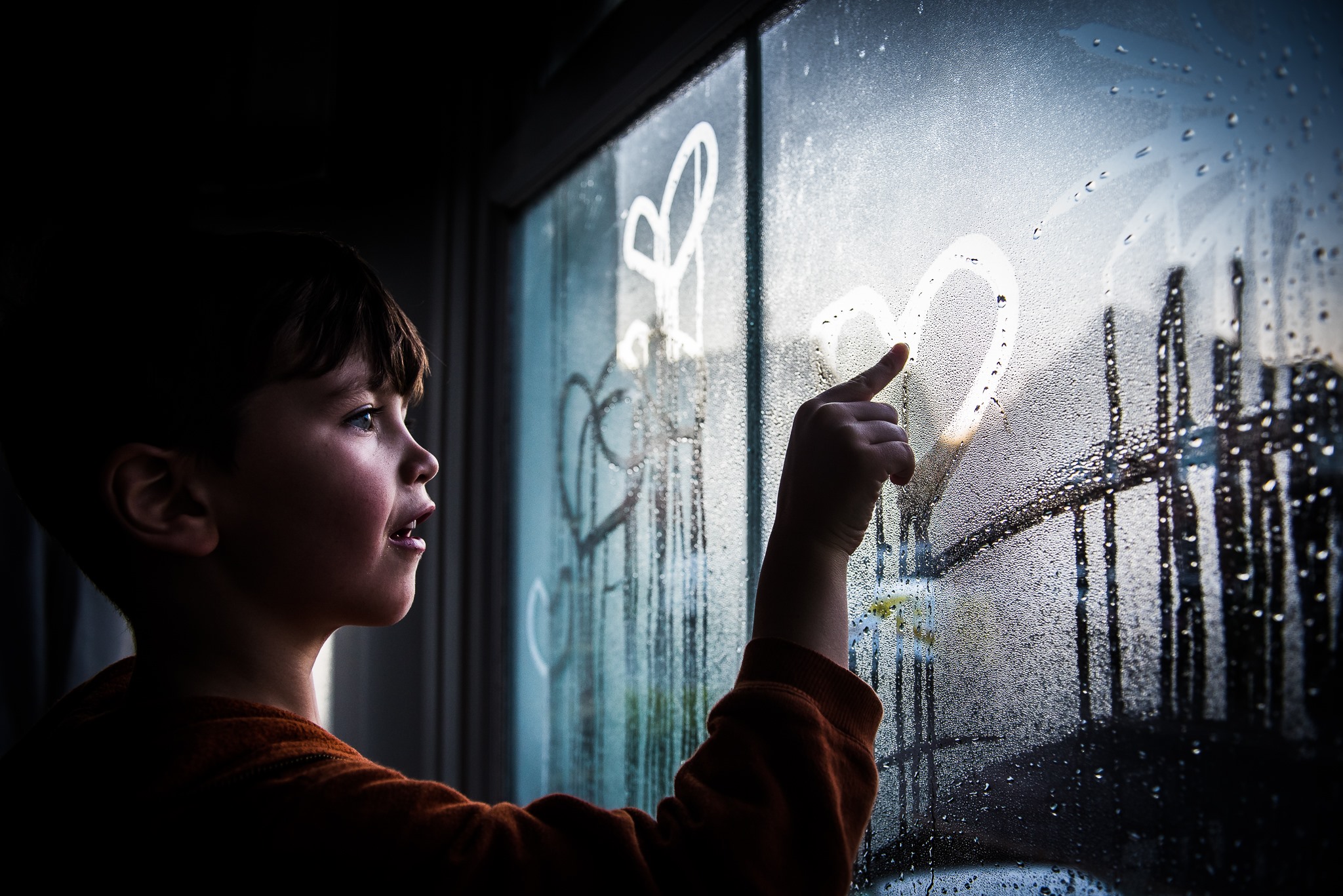 A kid drawing a heart shape in the condensation of a window pane