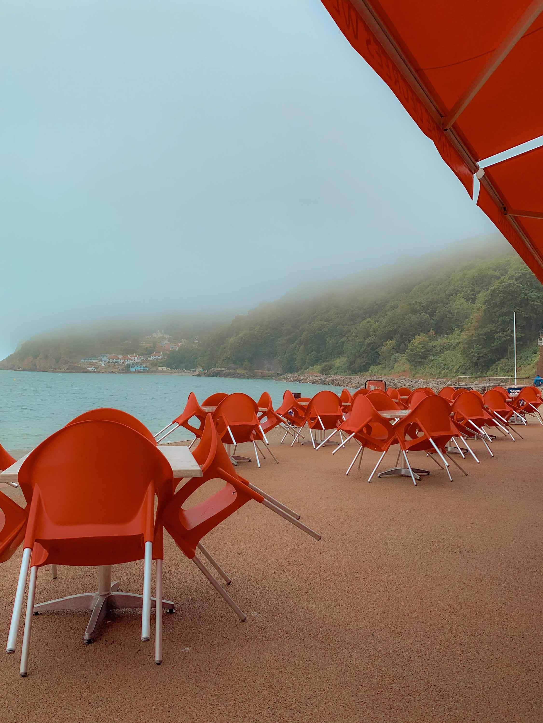 Red chairs stacked up on a misty seafront. Image by Josh Edgoose.
