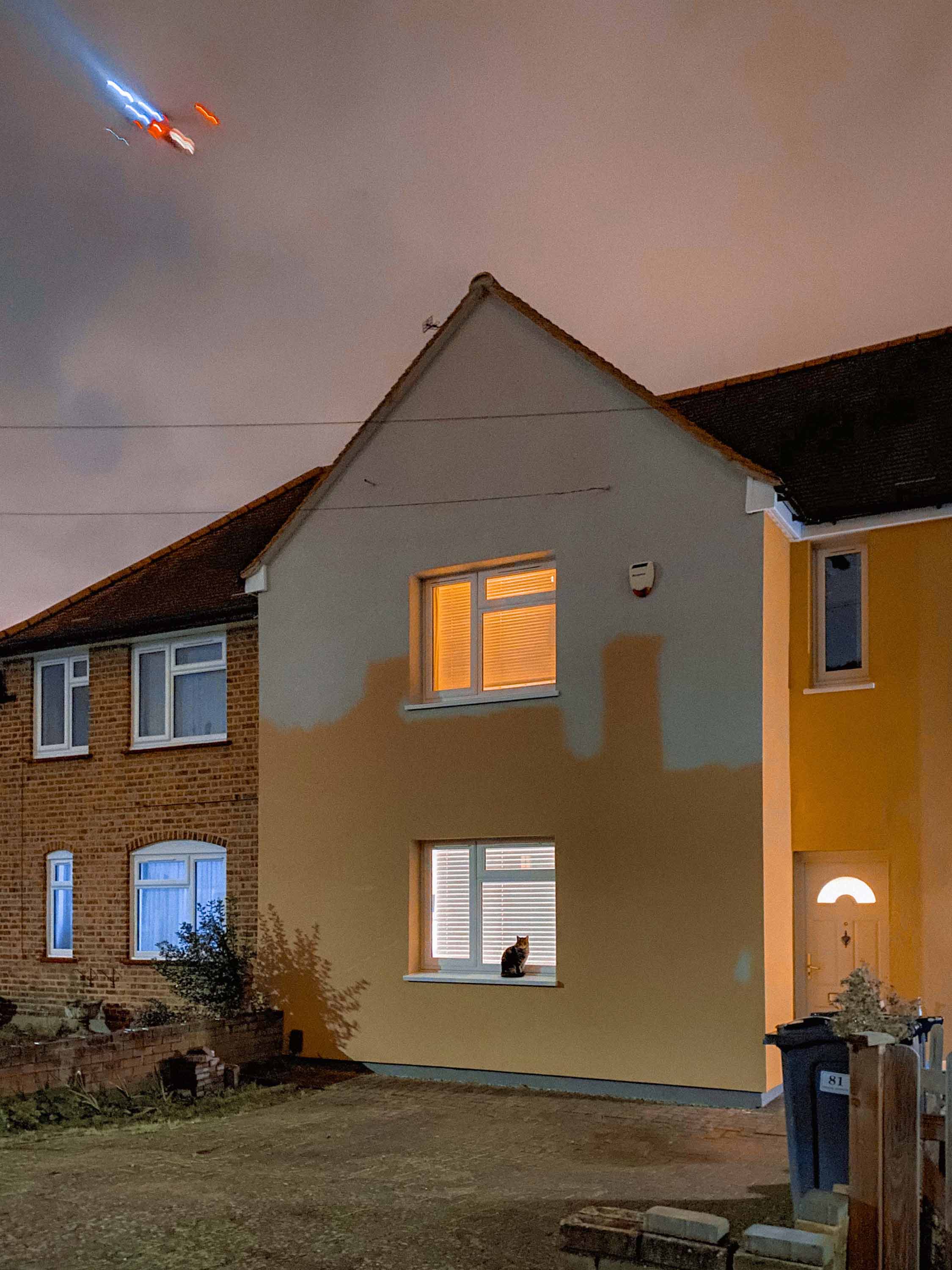 Night-time image of a half-painted house with a cat sitting on a windowsill. Image by Josh Edgoose.