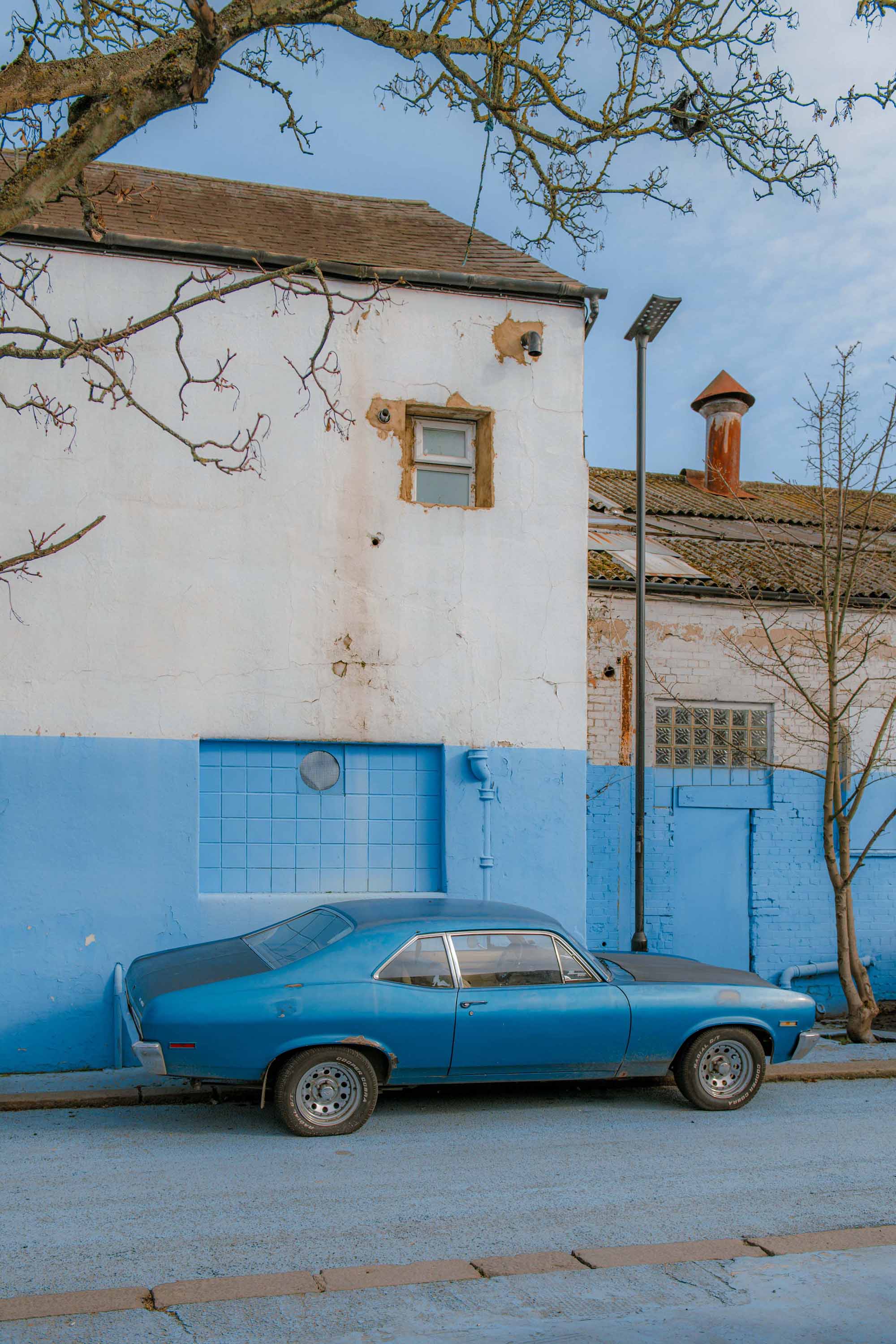 Old blue mustang car parked on the street, with a blue wall as a background. Image by Josh Edgoose.