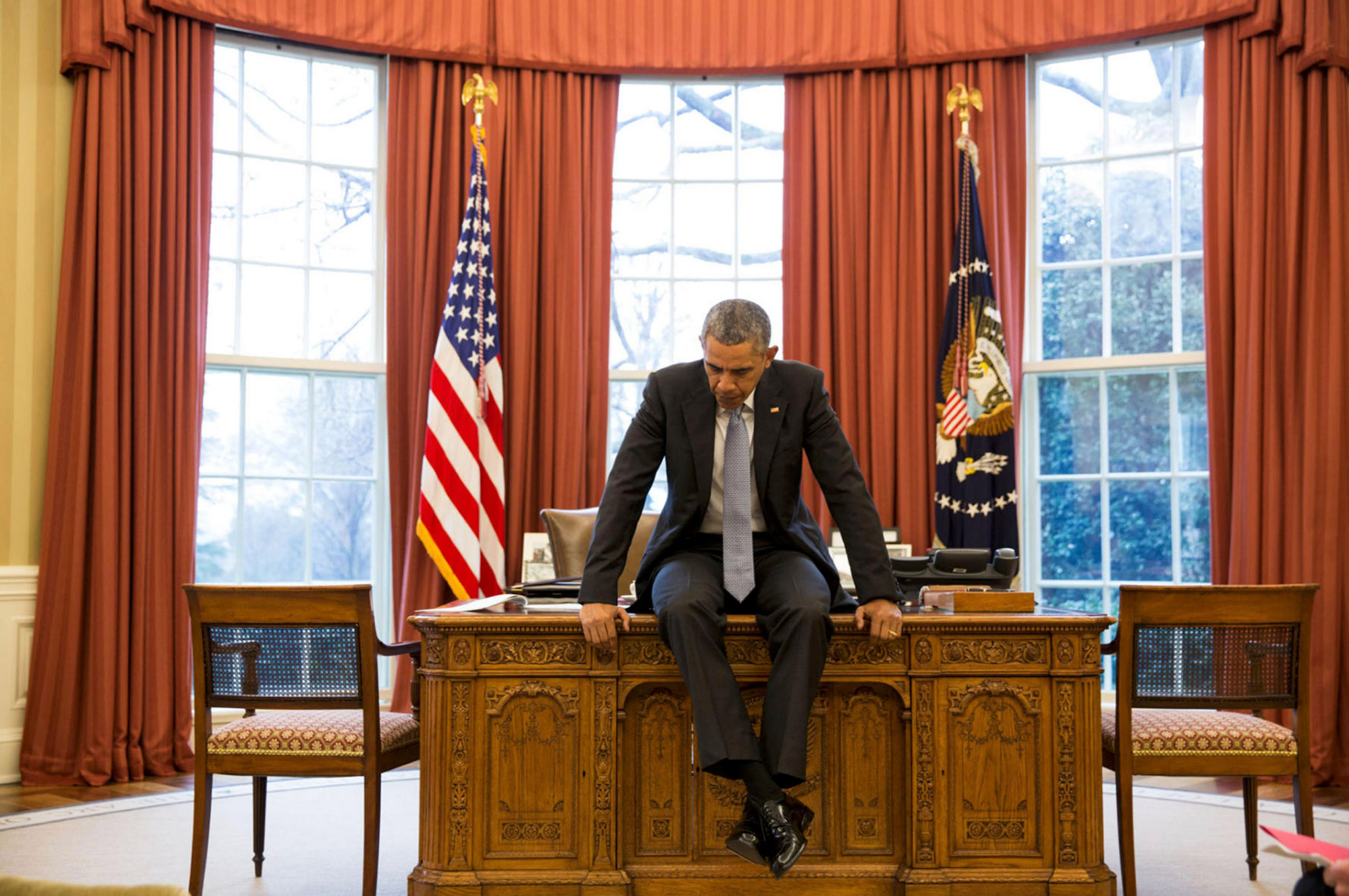 President Barack Obama sitting on the desk in the Oval Office