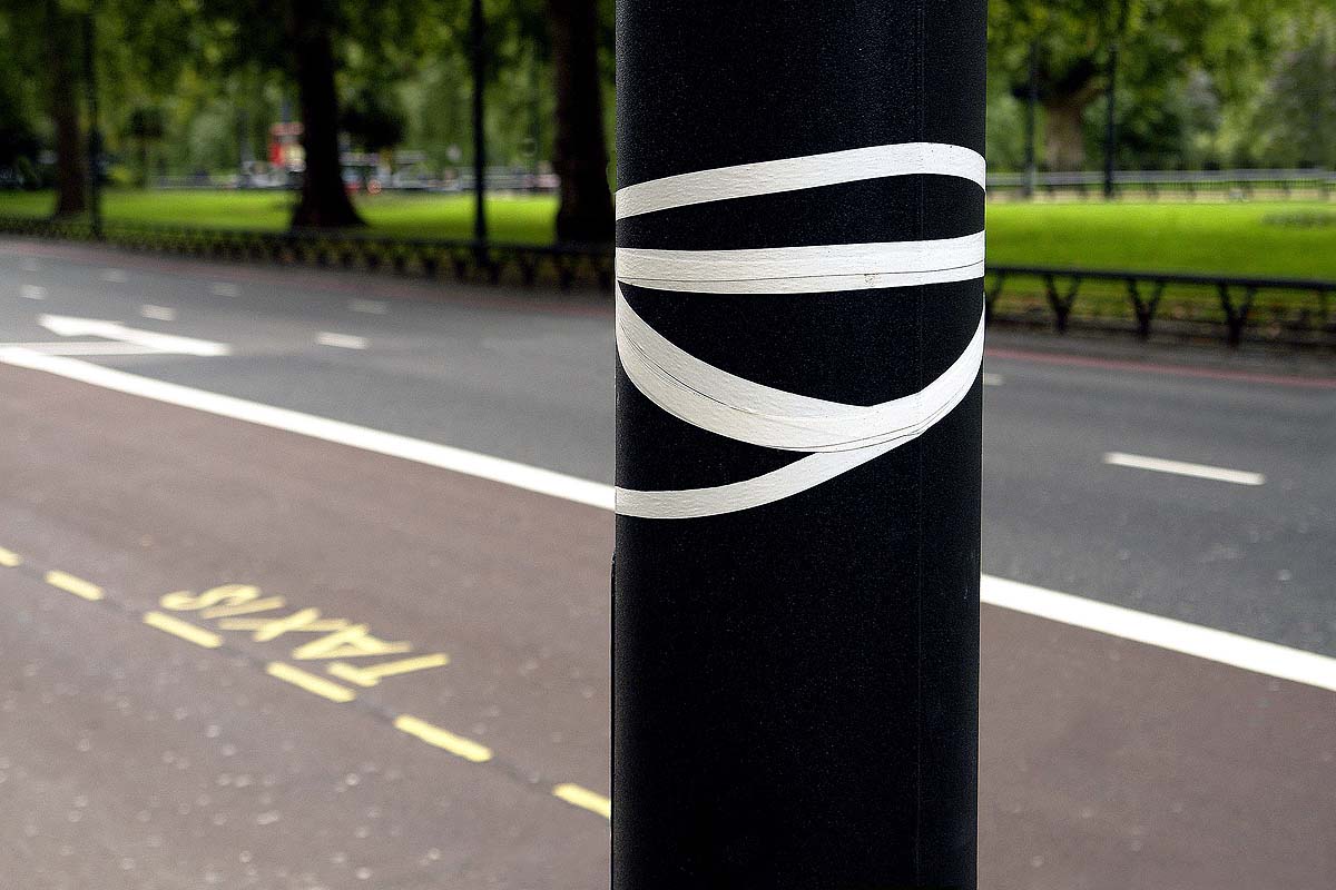 A black pole with white tape that matches the white stripes on the asphalt
