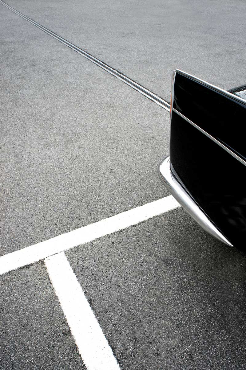 A black car whose silver lines perfectly match the line on the street.