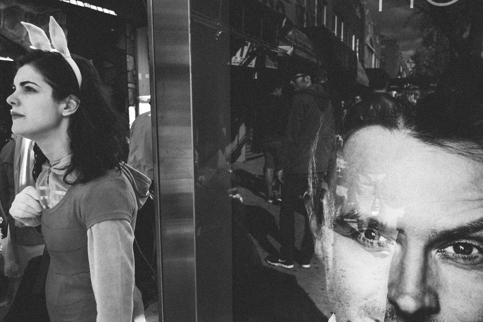 Person wearing bunny ears on the street with a big reflection and advertisement to the side