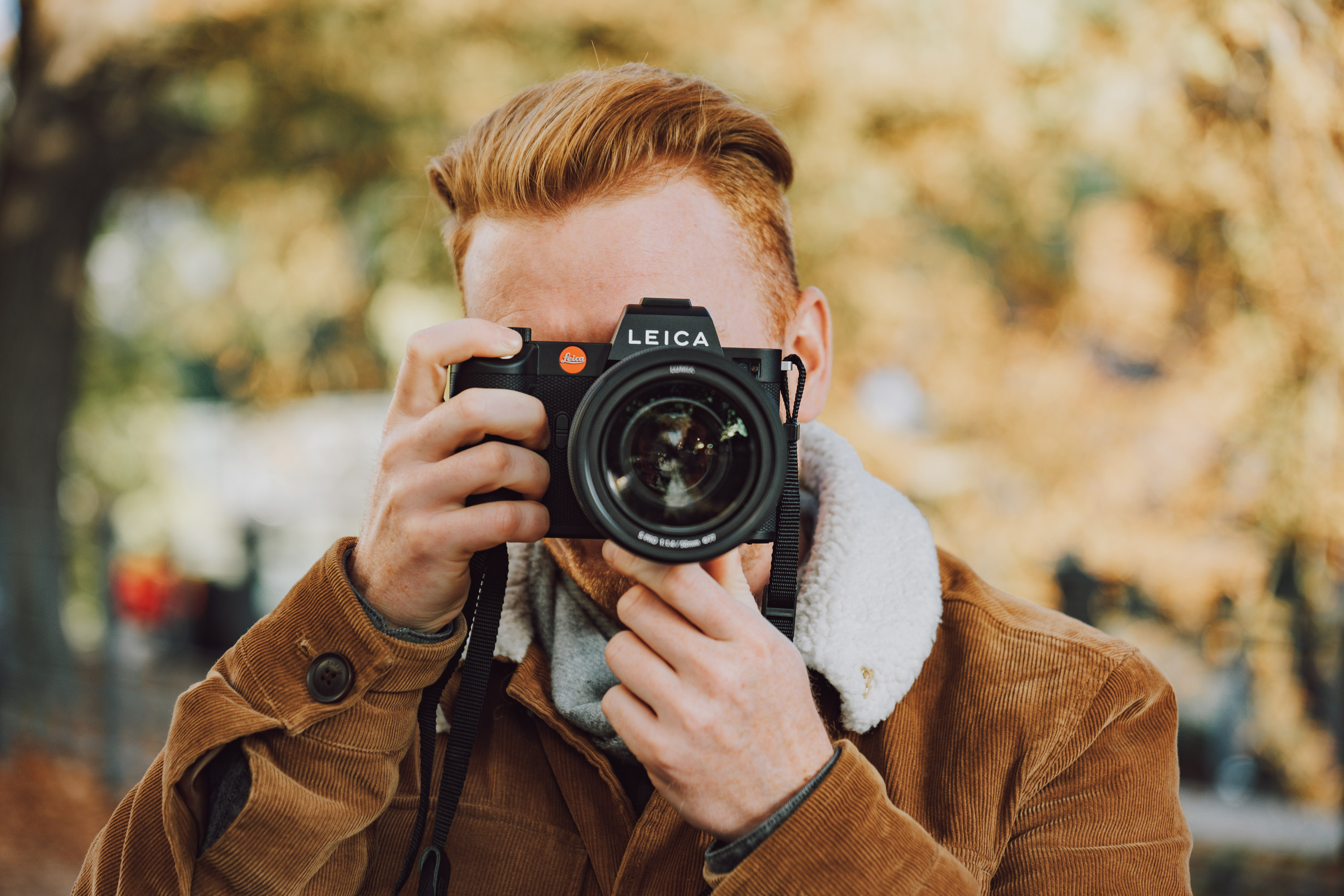 Een man in een bruine jas die een foto maakt met de Leica SL2