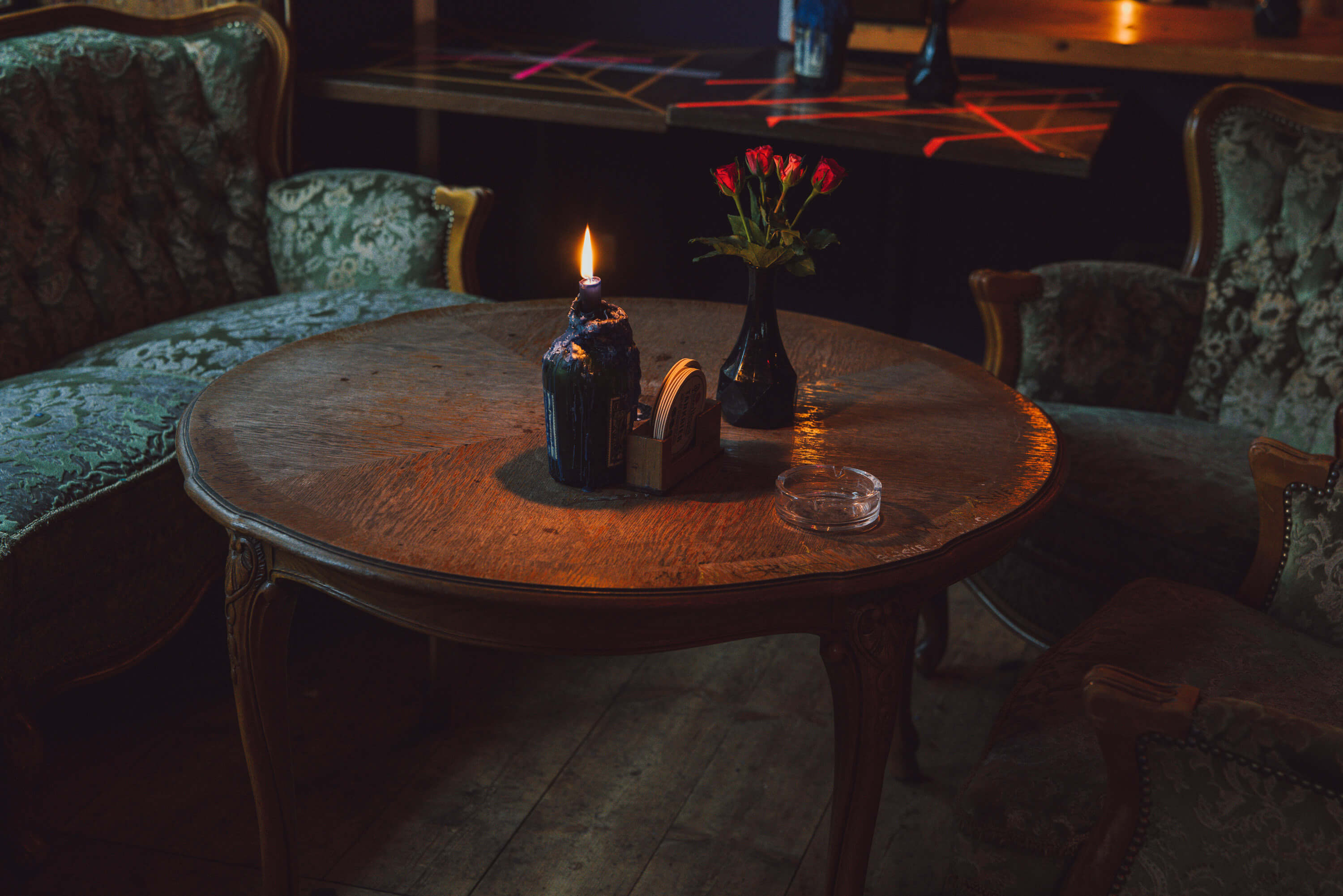 Afbeelding van een tafel met een brandende kaars en een vaas met rode rozen en een aslade