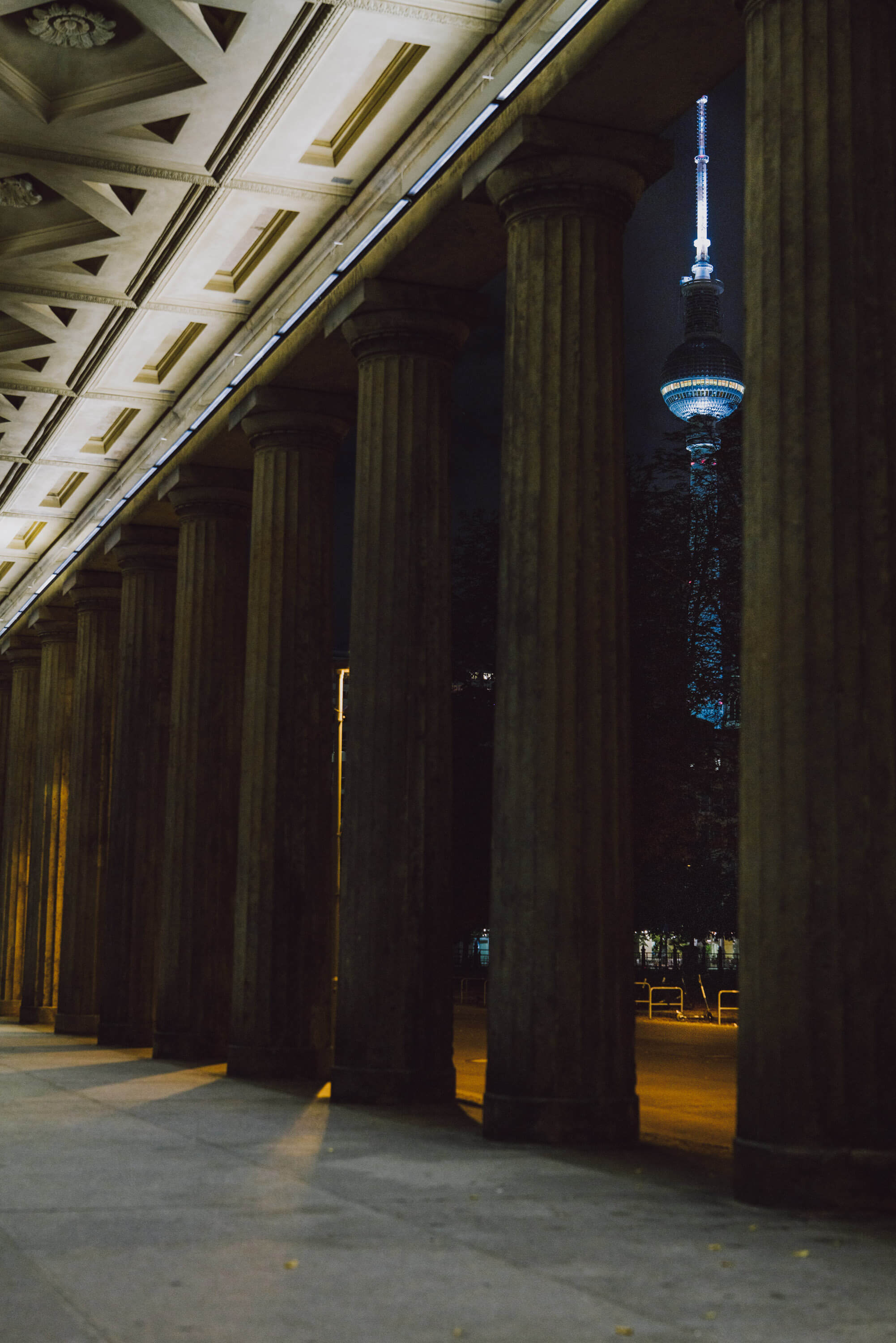Nahaufnahme von Säulen vor einem Museum bei Nacht, Berliner Fernsehturm im Hintergrund