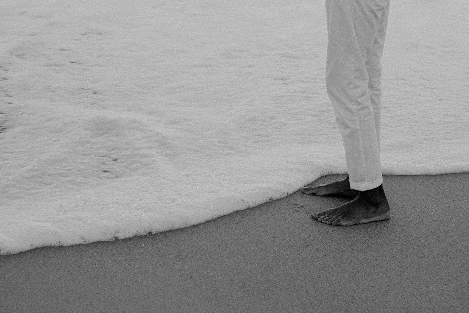 Black and white photo of feet and beach in foamy water