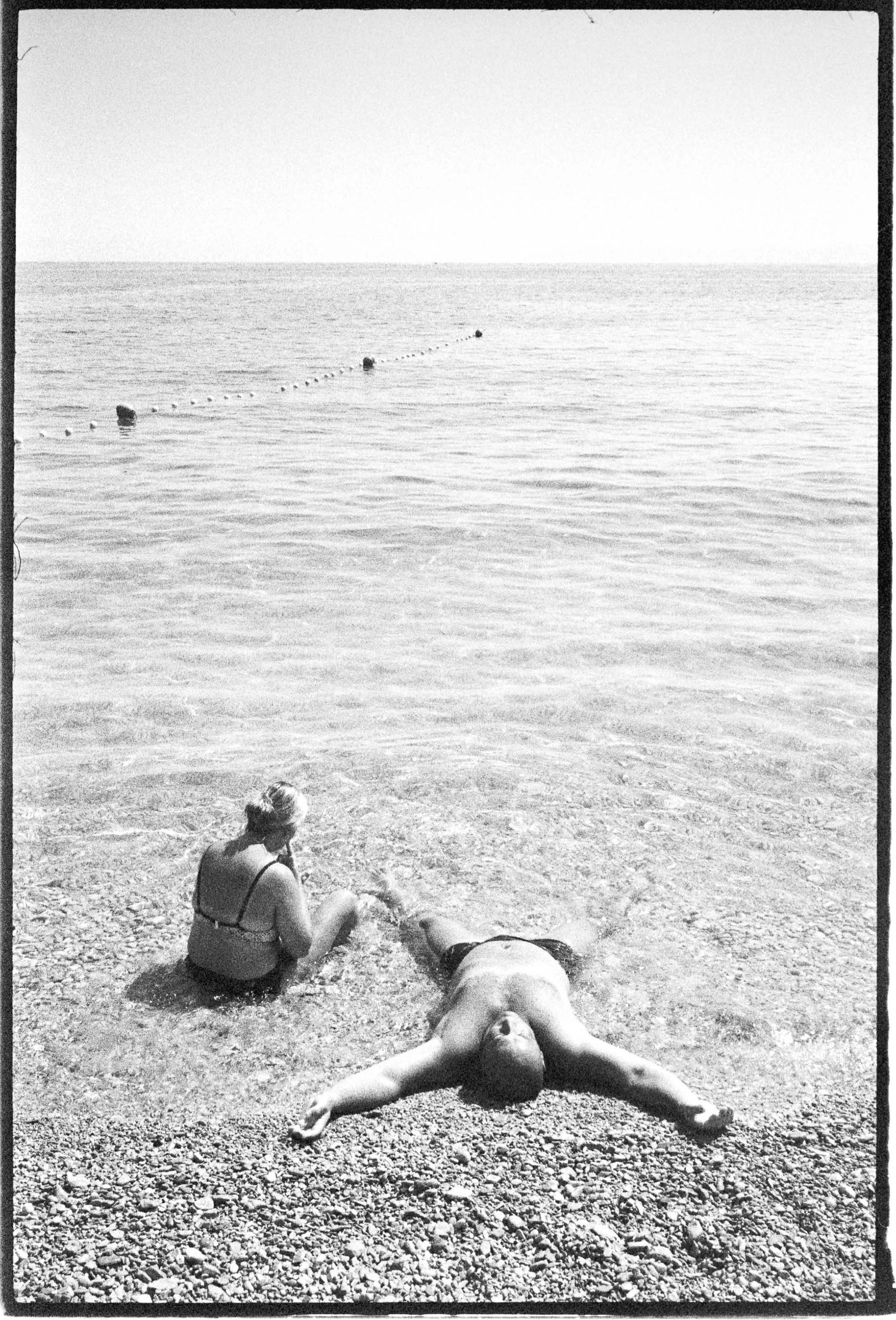 black-and-white photo of man laying in shallow beach water Brighton