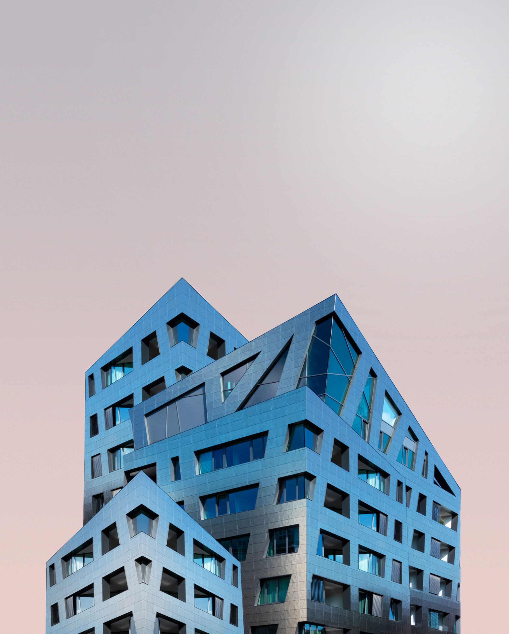 Blaues Gebäude mit interessanter geometrischer Form vor einem pastellfarbenen Hintergrund