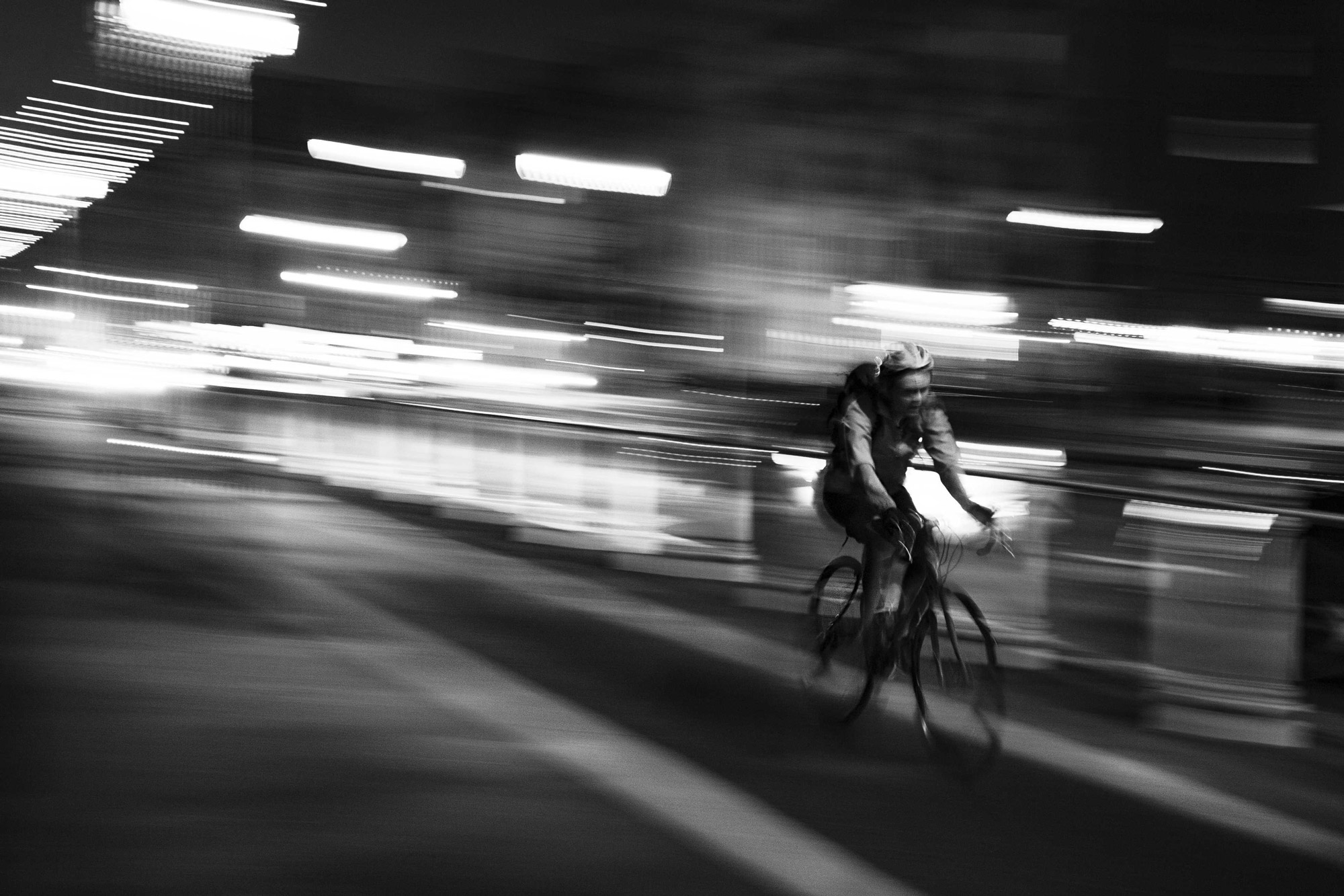 A black and white photograph of a cyclist. The shutter speed has been decreased, giving the image a blurred, action-type look.