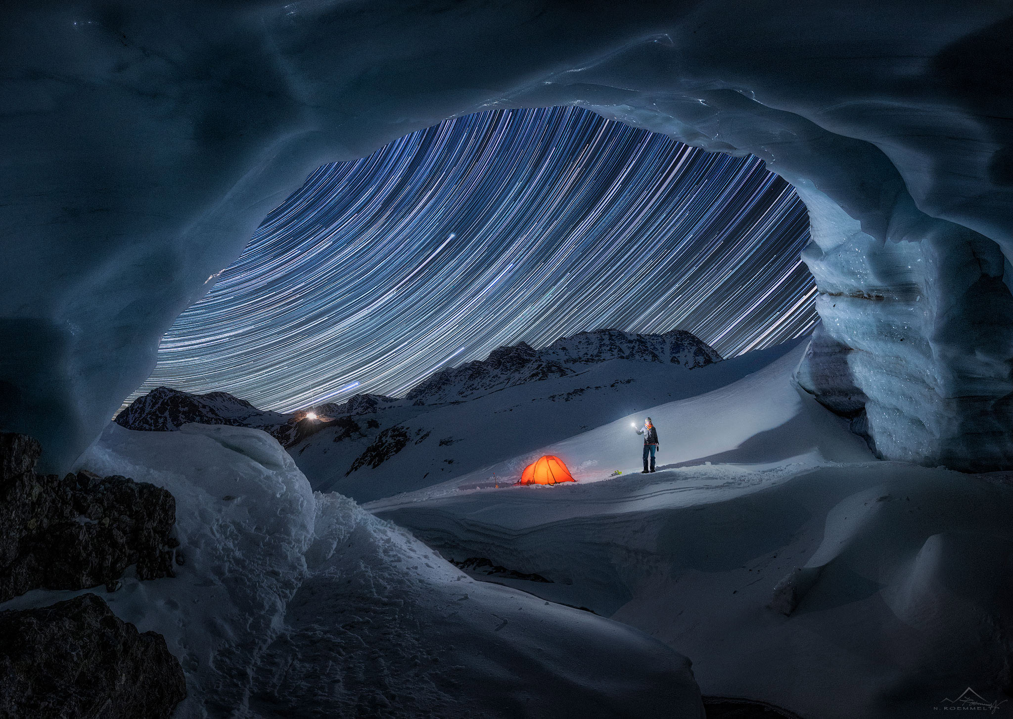 A photograph taken from a snowy landscape with stars moving across the sky. In this image, a low shutter speed has been used to create movement.