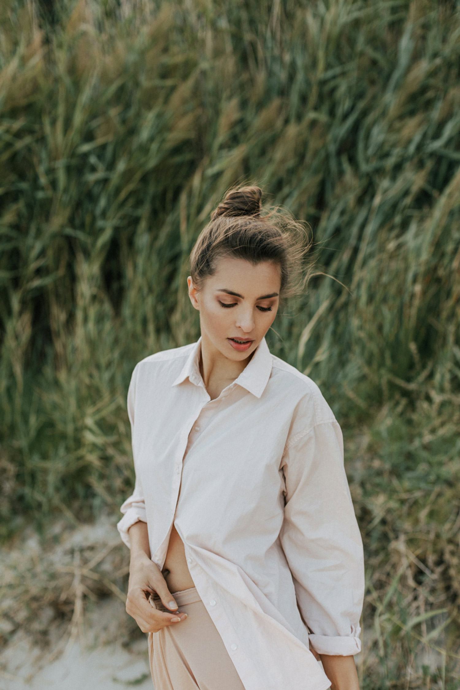 A woman posing in front of a hill with tall grass.