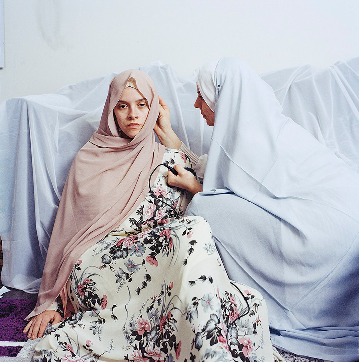 Woman posing for a portrait as another tends to her hijab. Jodie Bateman @jodiembateman.
