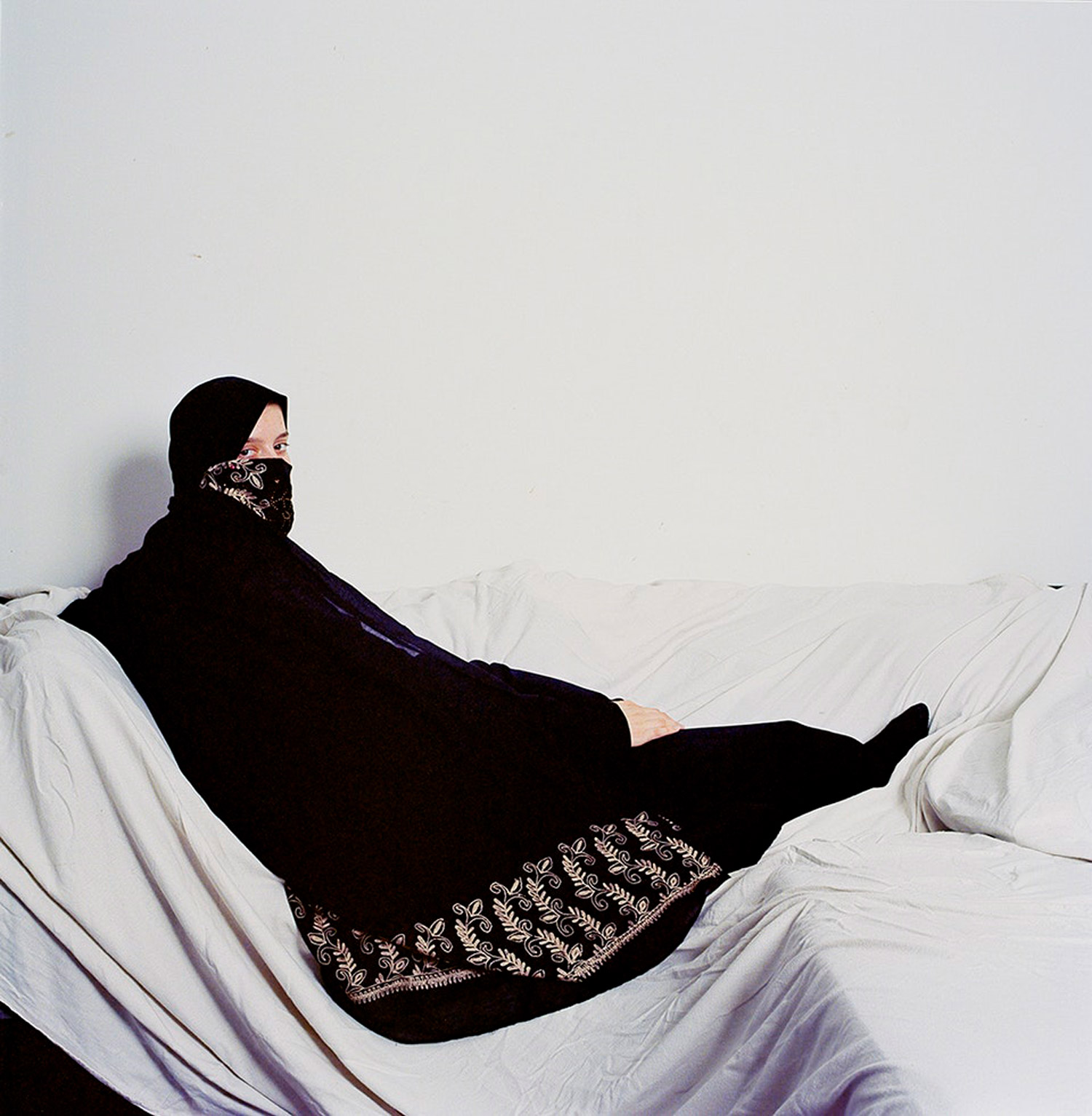 Woman in a black hijab posing on a sofa covered in a white sheet. Jodie Bateman @jodiembateman.