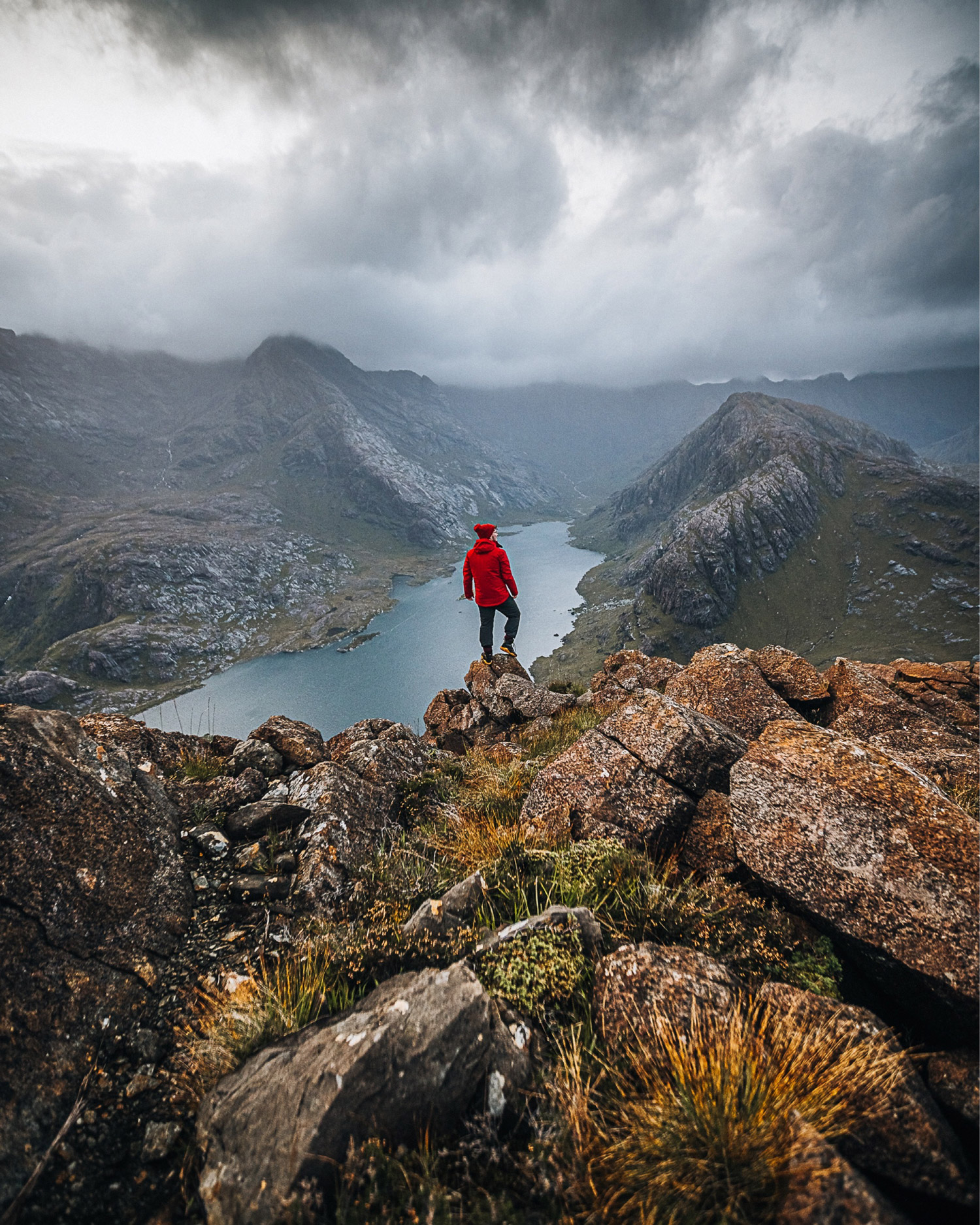 Person standing on a cliff edge overlooking a stunning mountainous landscape 