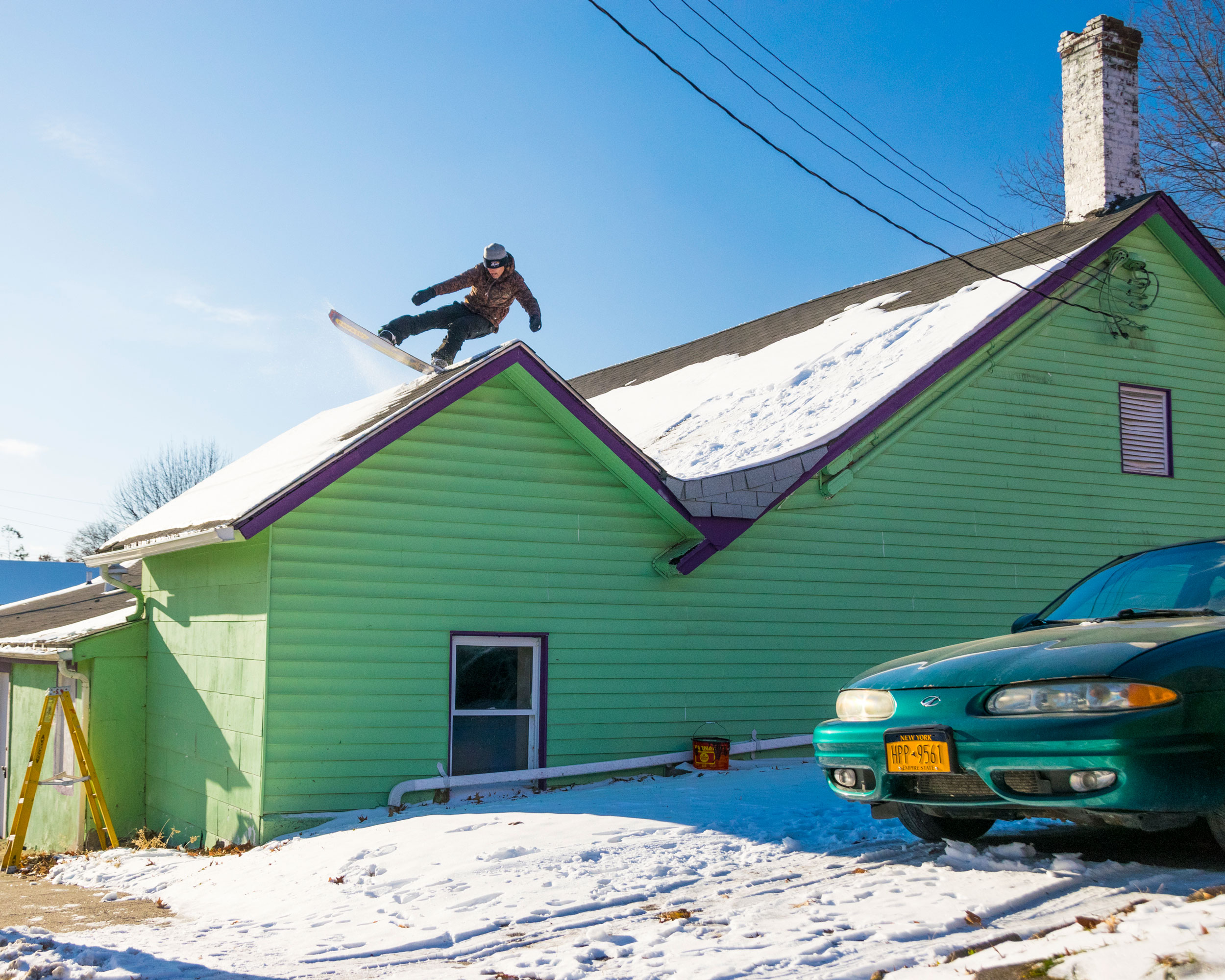 Snowboarder on top of green snowy house. Shot by Jon Mecca.