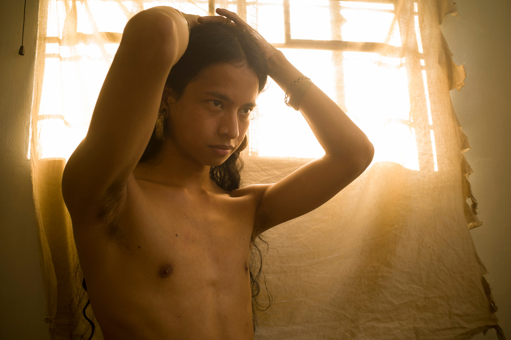 A person with hands on their head, with the sun shining through the window behind them. Shot by Regine David. 