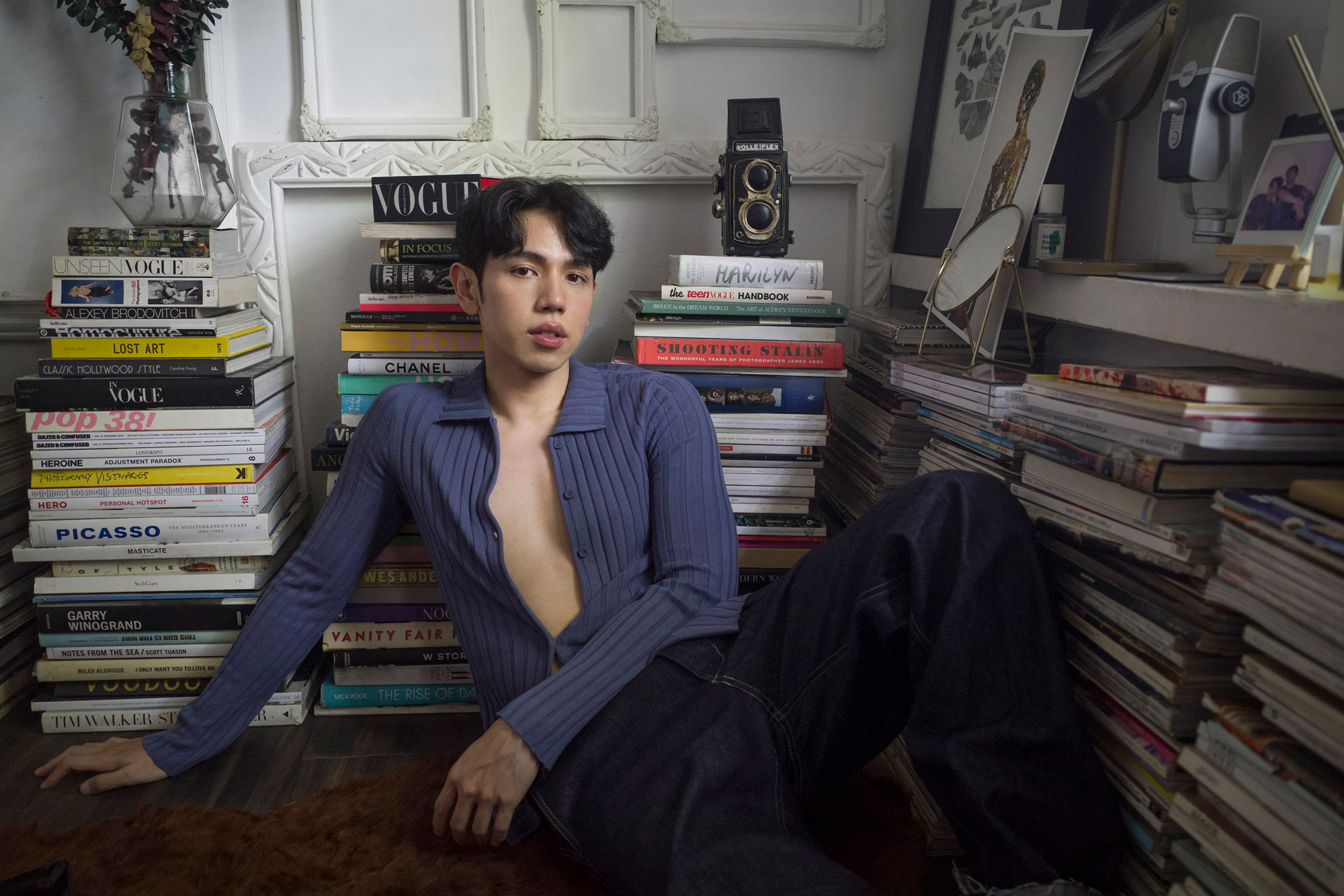 A person posing in front of a stack of books. Shot by Regine David. 