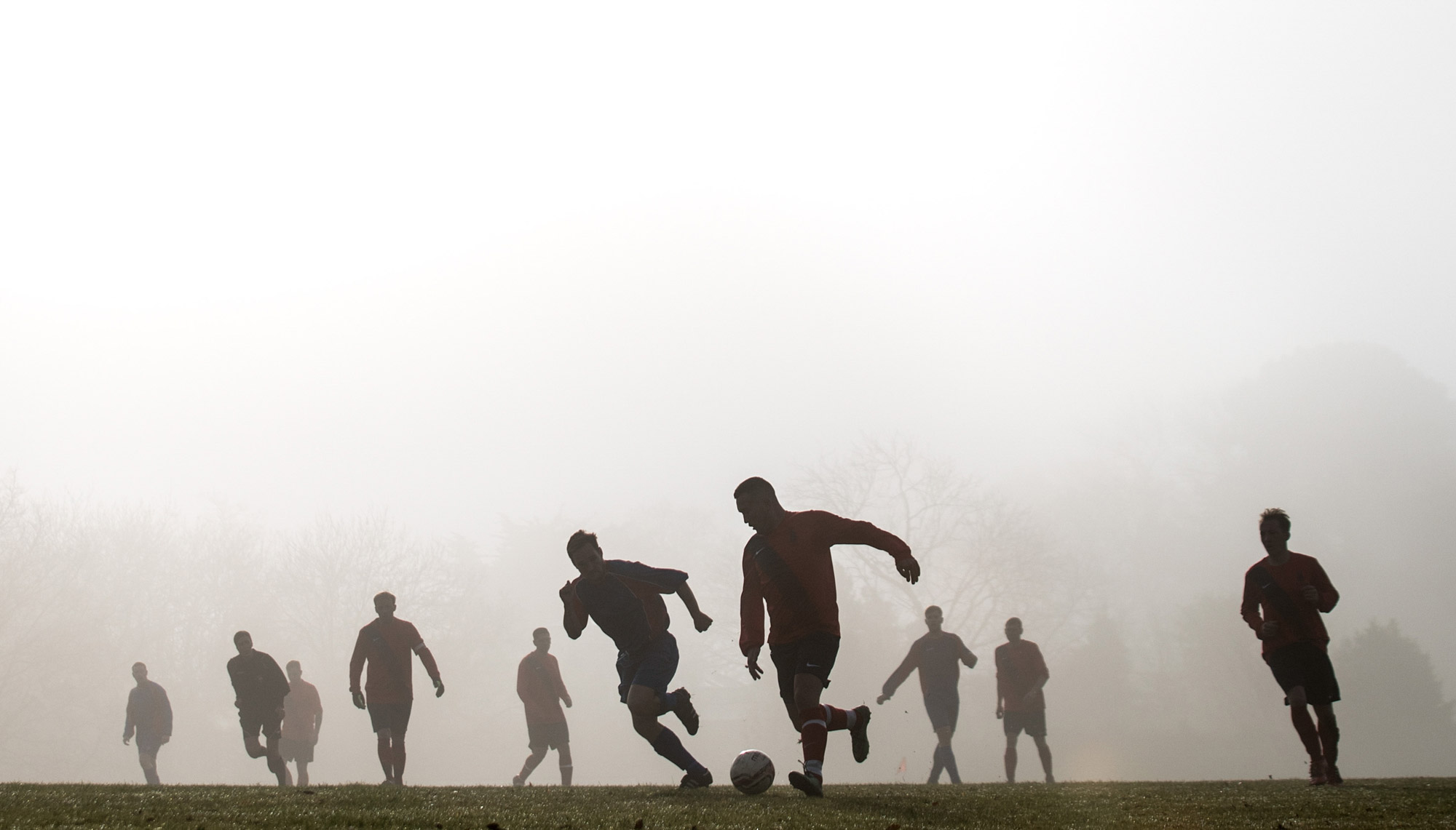 Football players playing on a misty pitch, silhouetted