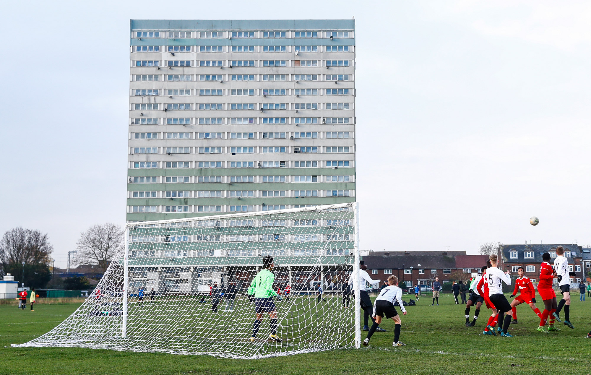 Youth football game in the foreground with a block of brutalist flats in the background