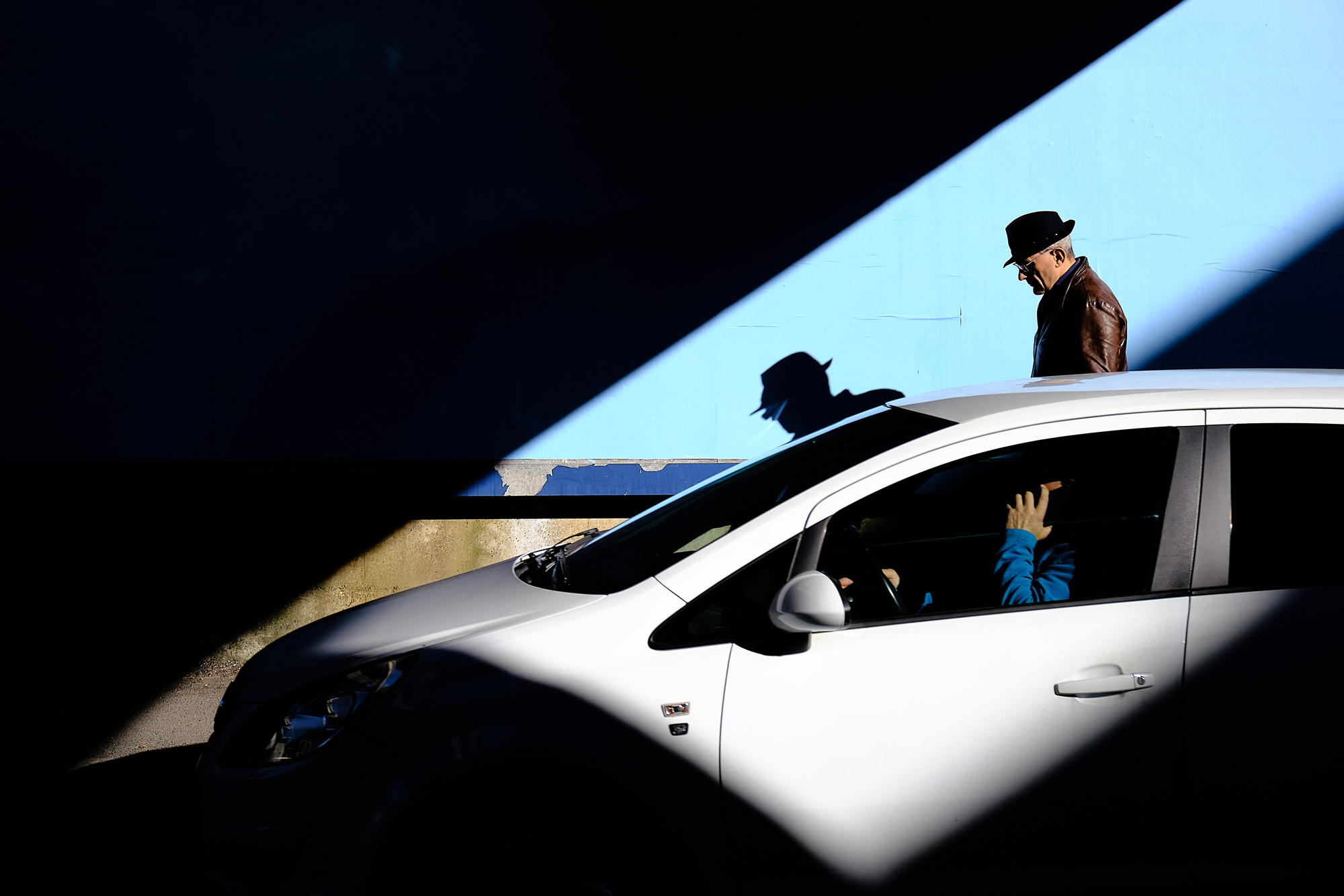 A man wearing a hat walking beside a white car.