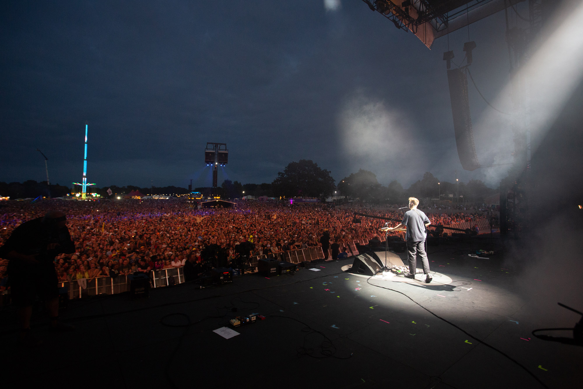 a photo taken from backstage at a festival at night, spotlight on the singer playing the guitar