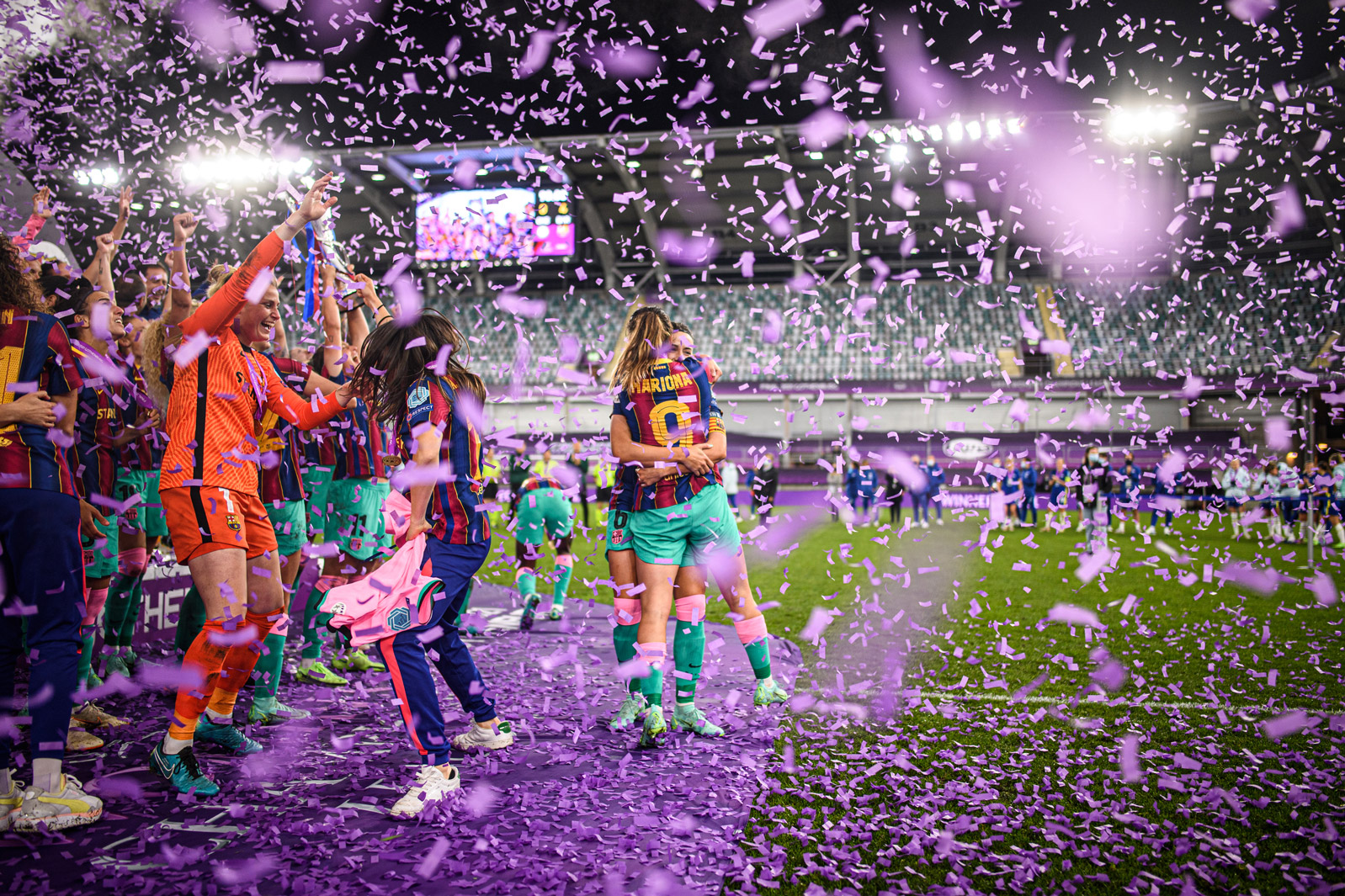 Football players celebrating their win in the stadium while being surrounded by pink confetti 