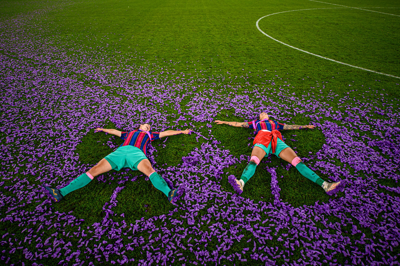 Ein Foto von zwei Fußballspielerinnen, die in einem Stadion auf dem Boden liegen, während sie von rosa Konfetti umgeben sind