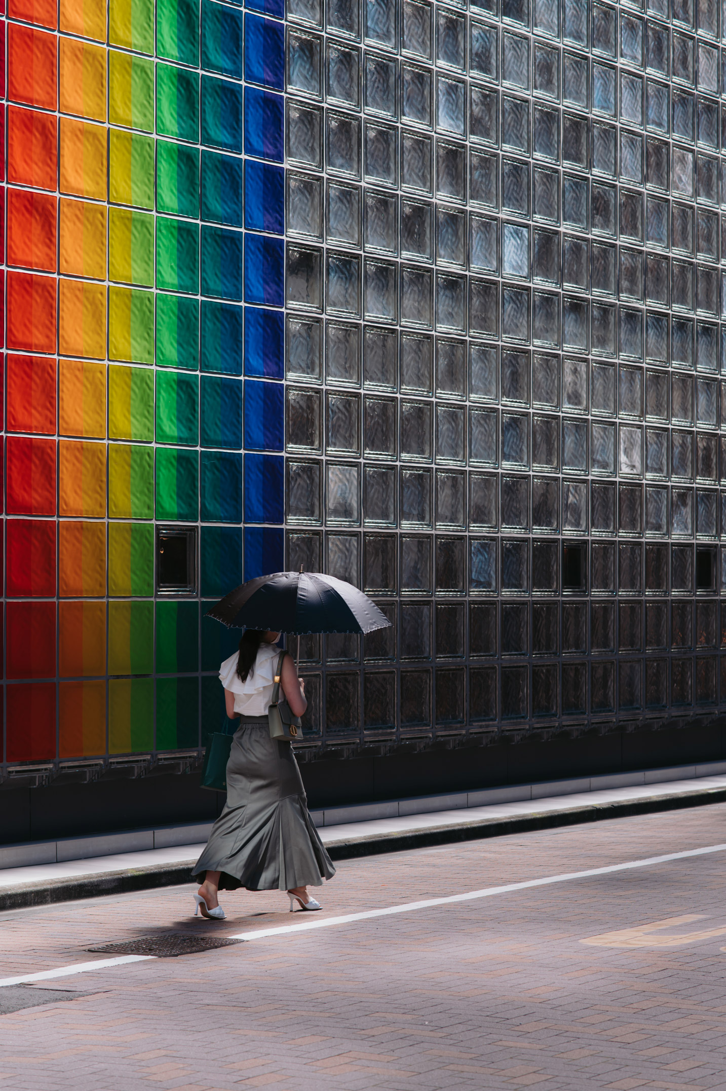 Eine Dame mit Regenschirm geht an einer Wand aus Regenbogenglas vorbei 