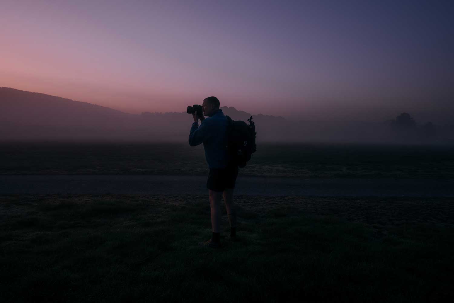 Fotograf macht ein Landschaftsfoto in der Abenddämmerung mit blau-rosa Sonnenuntergang 
