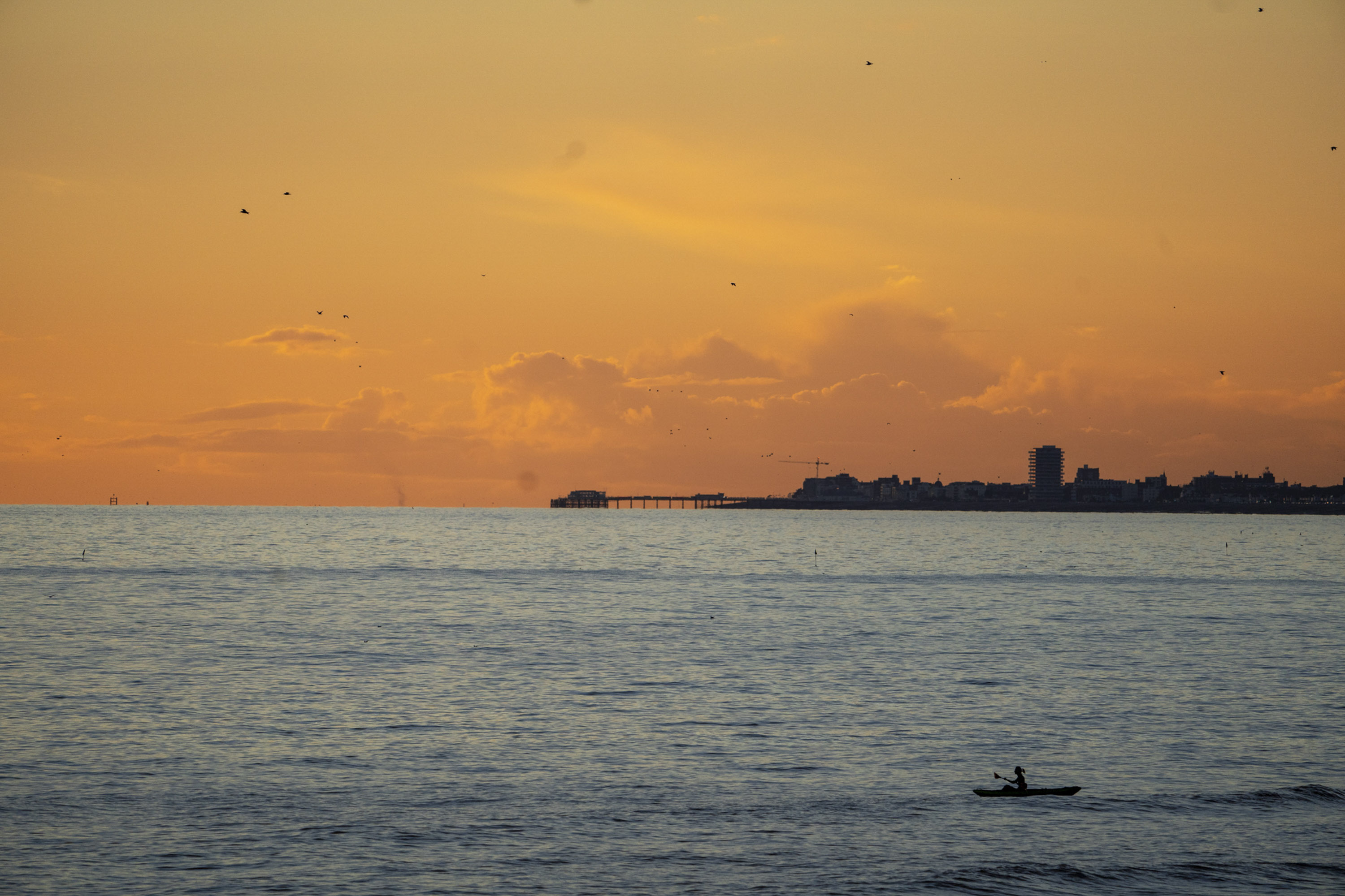 Kayaker at sea with an orange sunset in the background, Brighton pier can also be seen in the far distance 