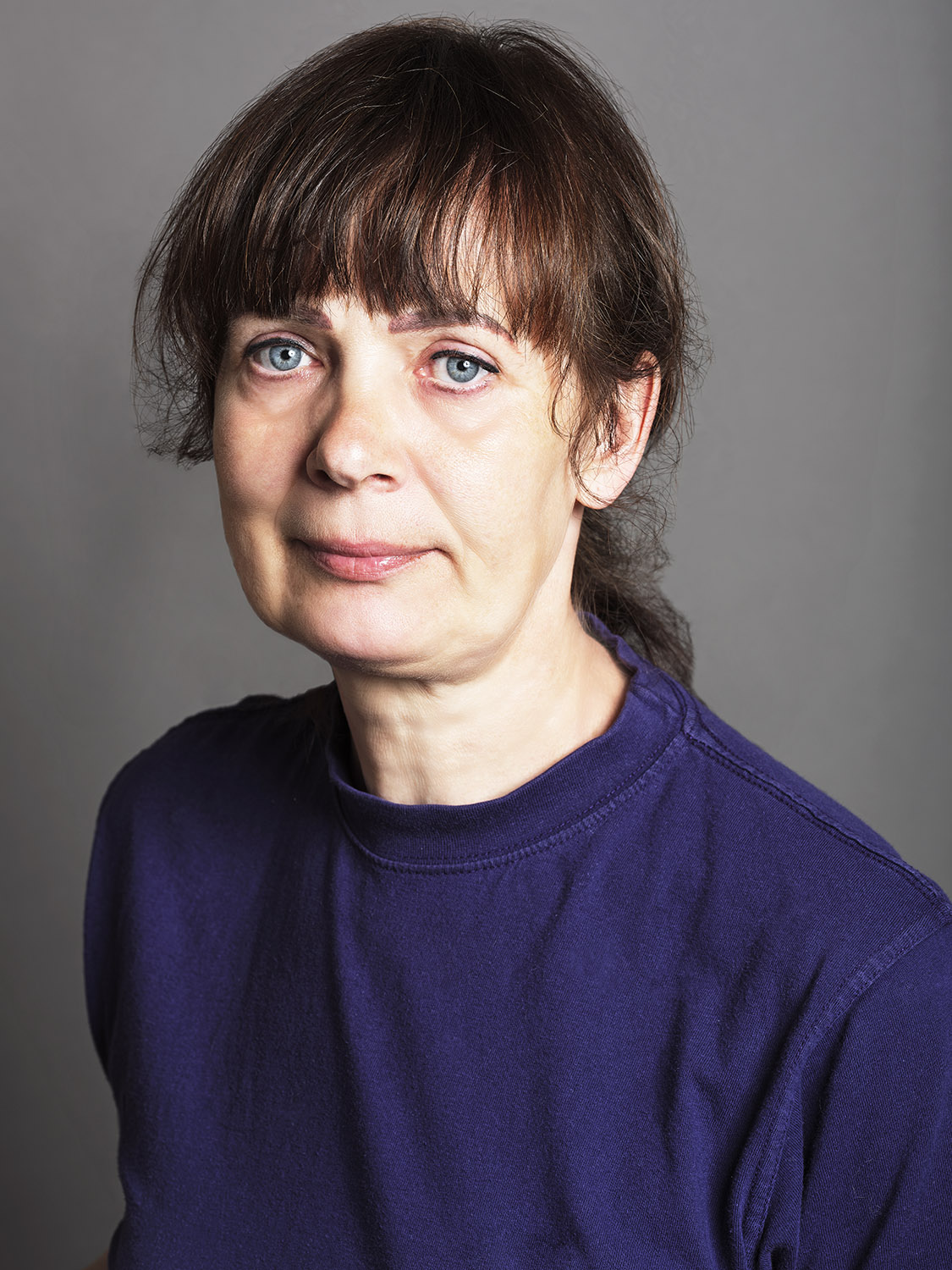 A portrait of a lady with brown hair wearing a blue top