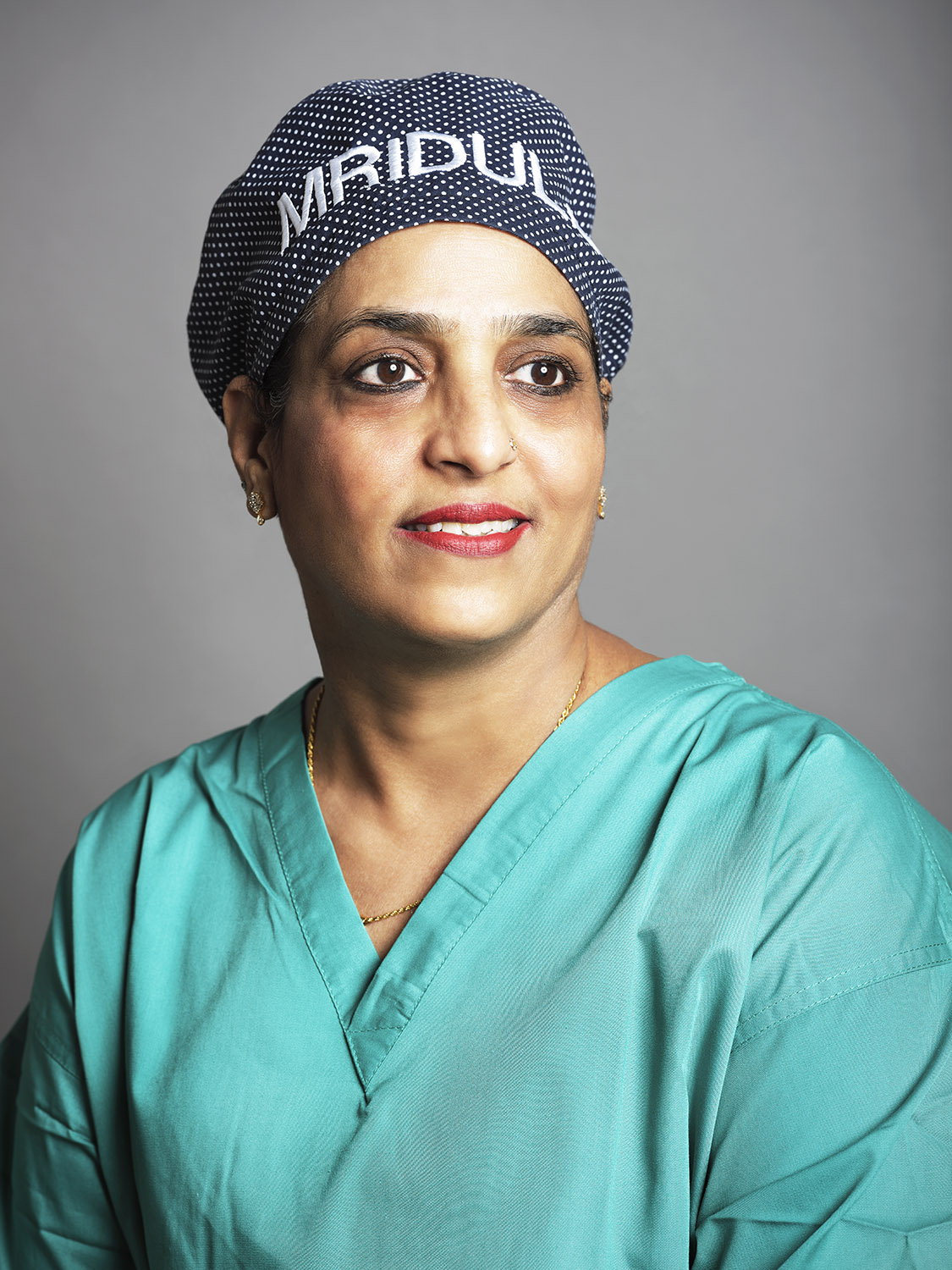 A portrait of a doctor with hair cap wearing green scrubs