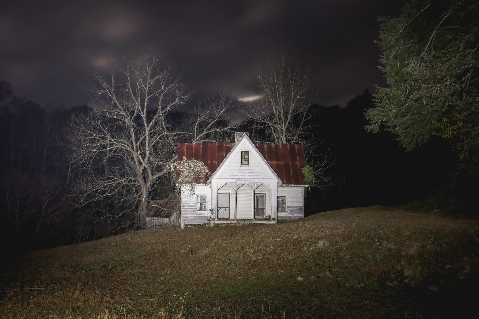 A small abandoned house with a tree at the side of it at night time